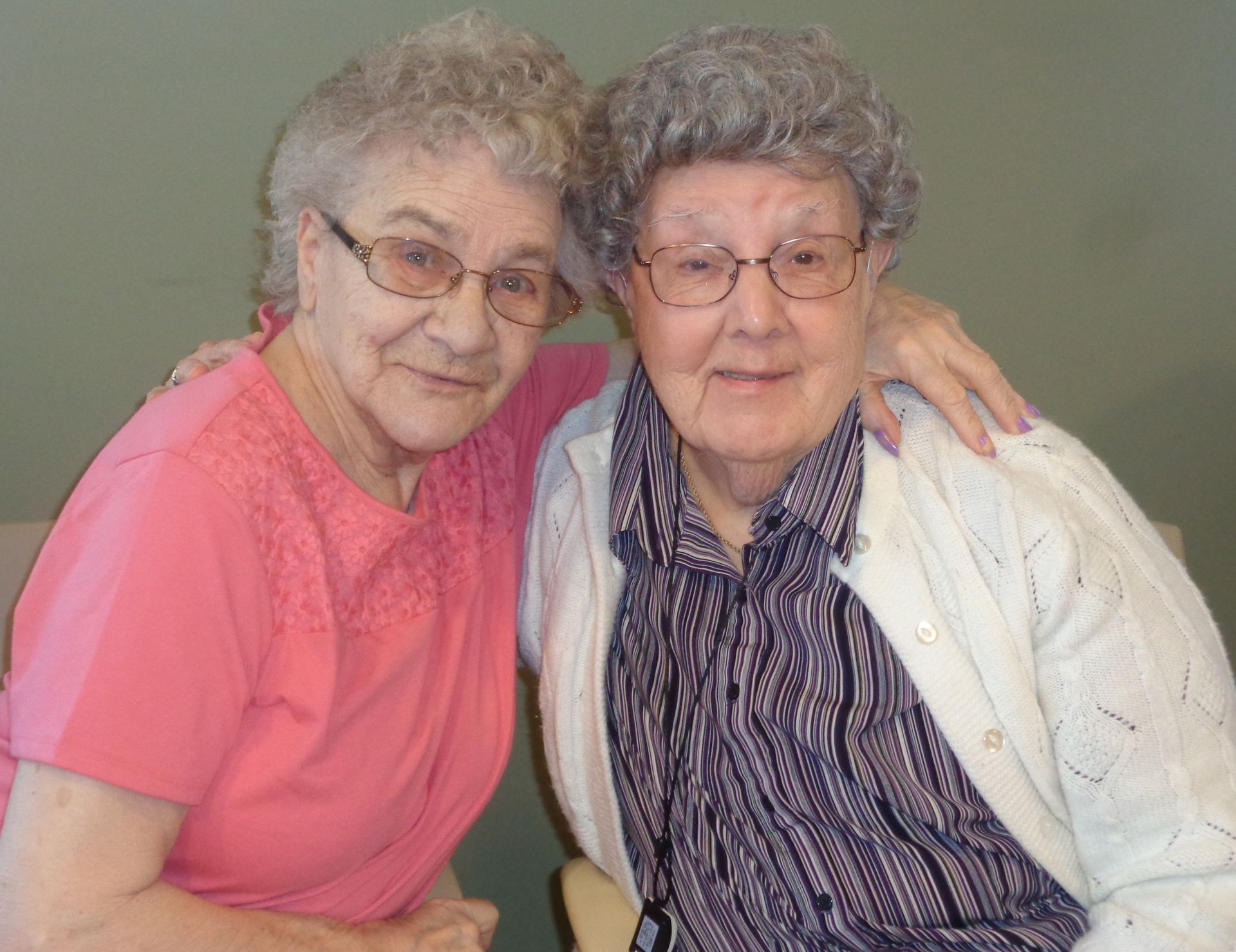 Two older women are posing for a picture together and one has her arm around the other 's shoulder.