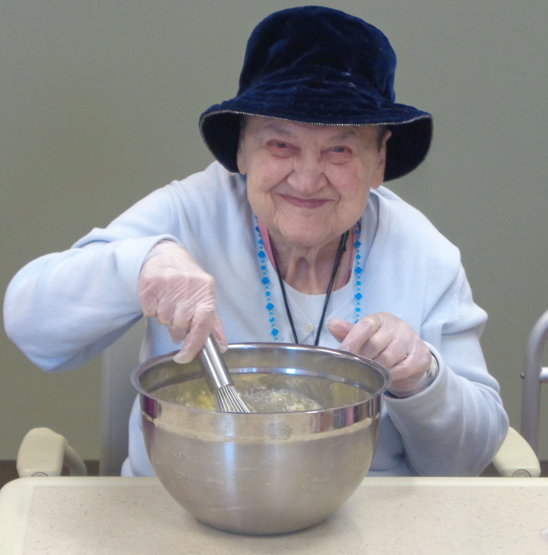 An elderly woman wearing a hat is mixing something in a bowl