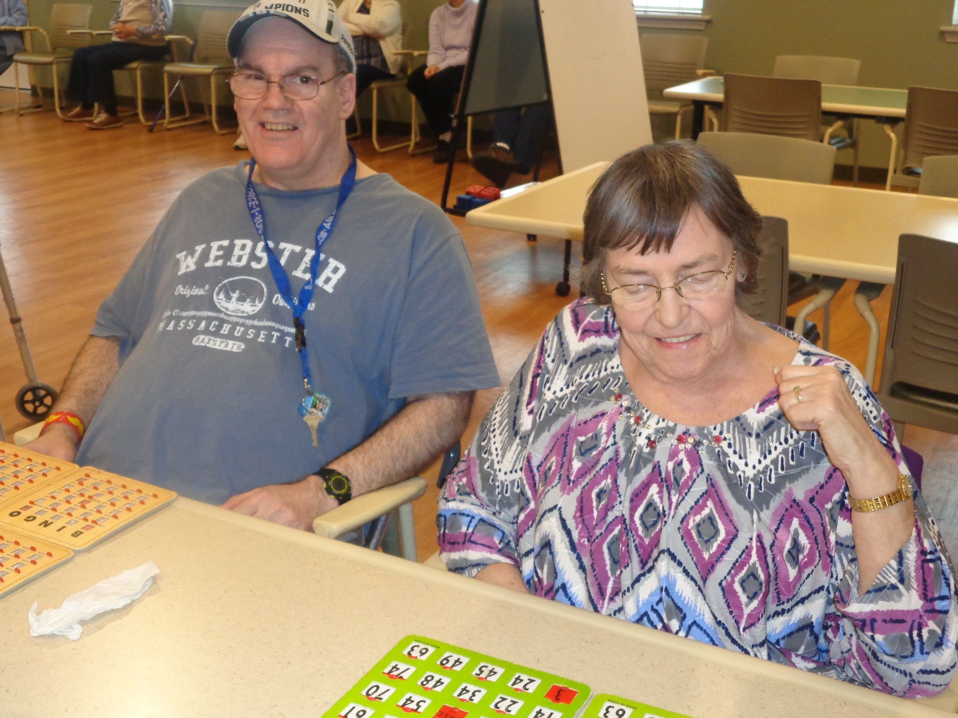 A man wearing a webster shirt sits next to a woman playing bingo