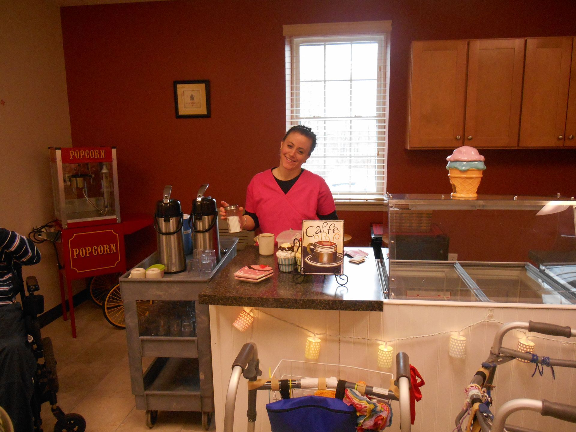 A woman in a pink shirt is standing behind a counter in front of a popcorn machine.