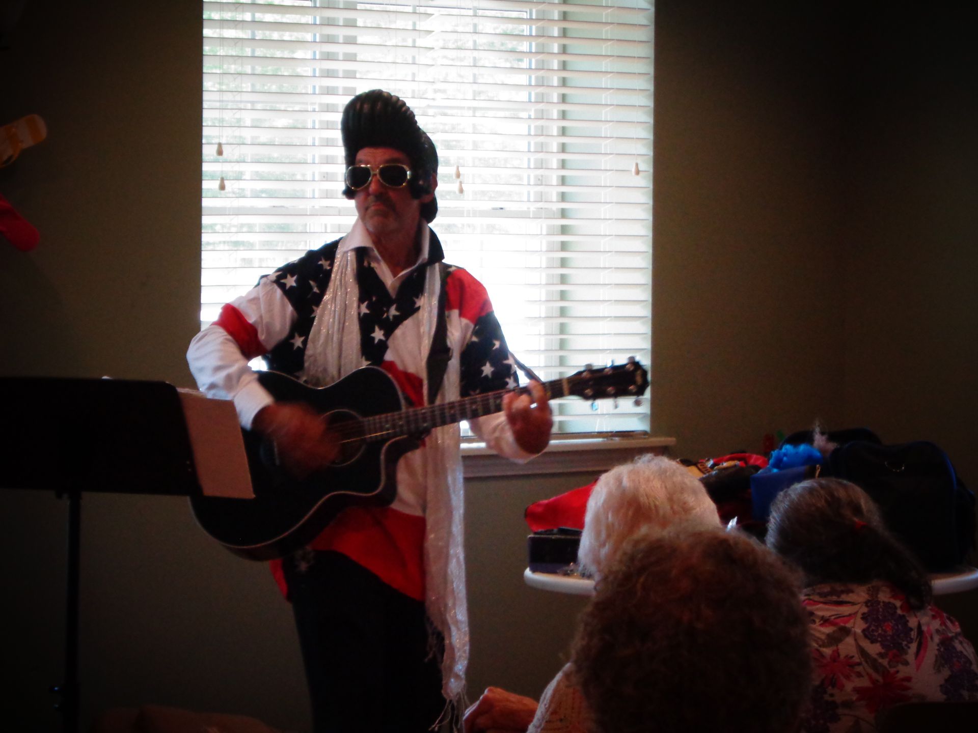 A man in an american flag outfit is playing a guitar in front of a window.