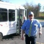A man with a cane is standing in front of a bus.