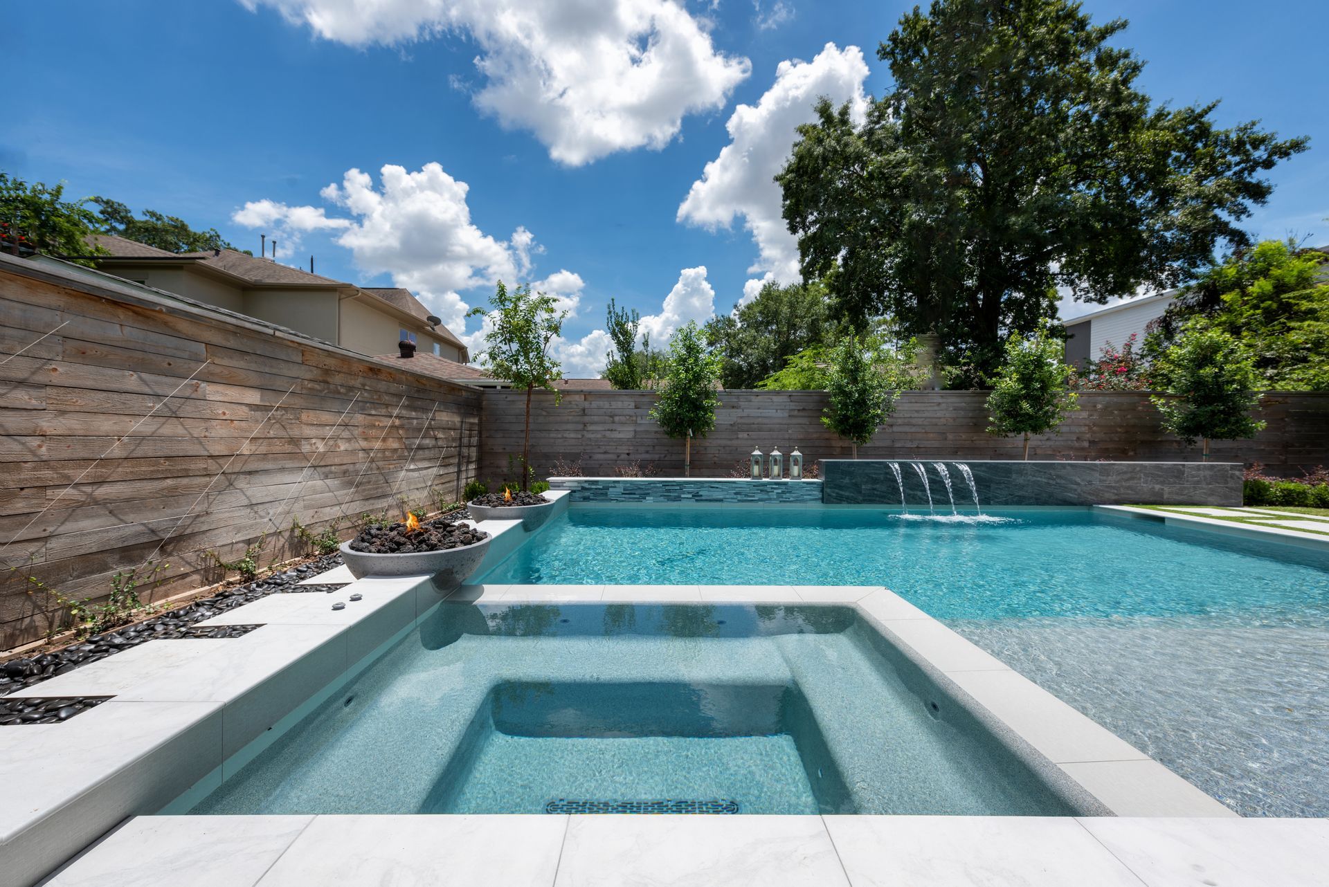 Outdoor pool with clear blue water, submerged lounge chairs, and trees under a bright blue sky