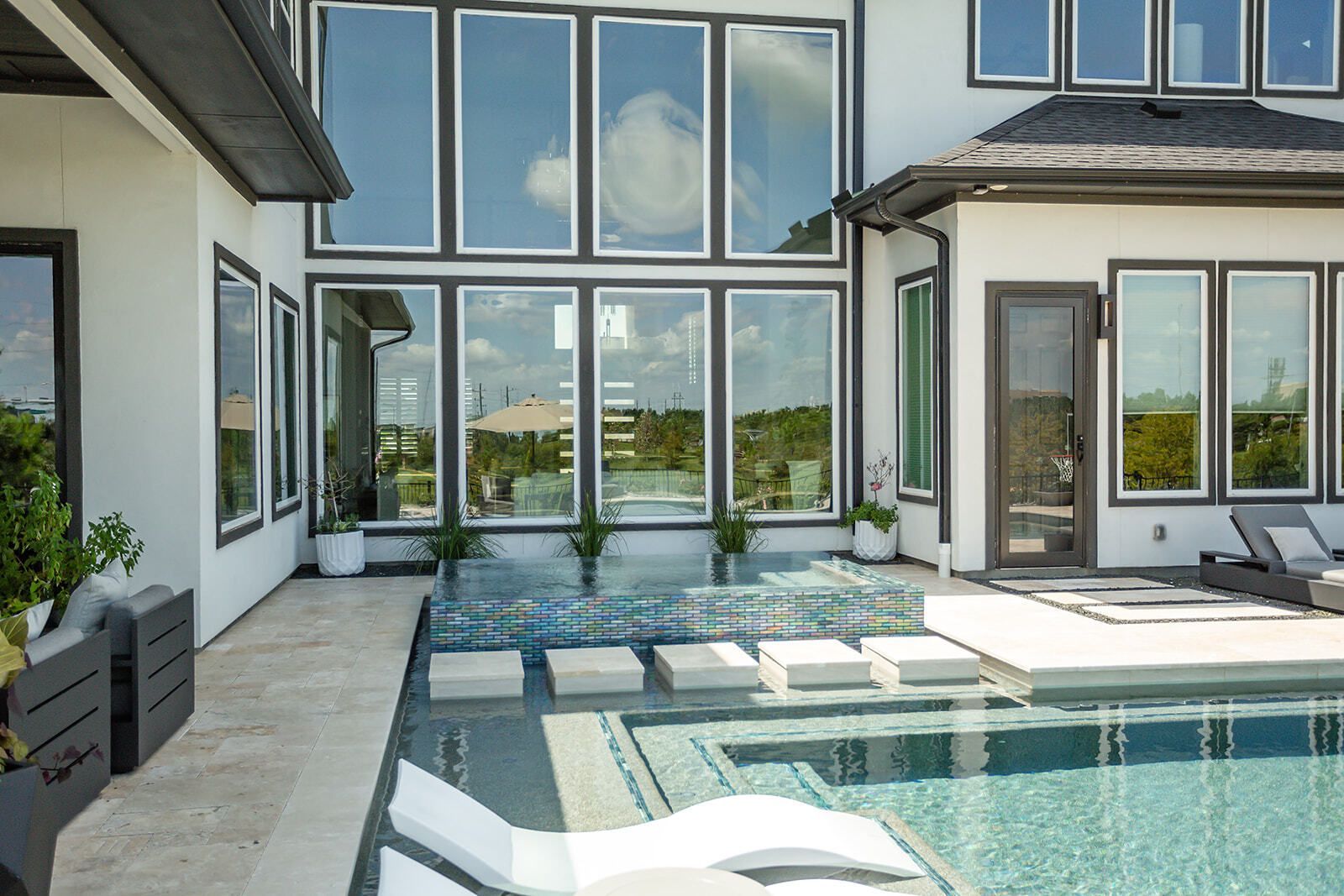 Backyard pool with a square hot tub, stone deck, and tall trees in the background.