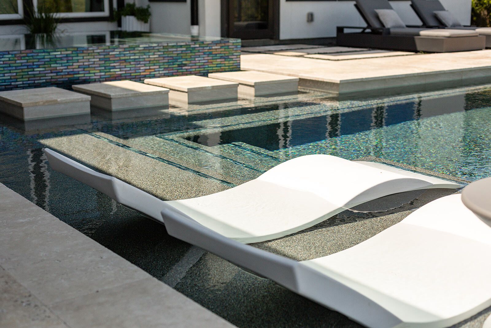 Backyard pool with a square hot tub, stone deck, and tall trees in the background.