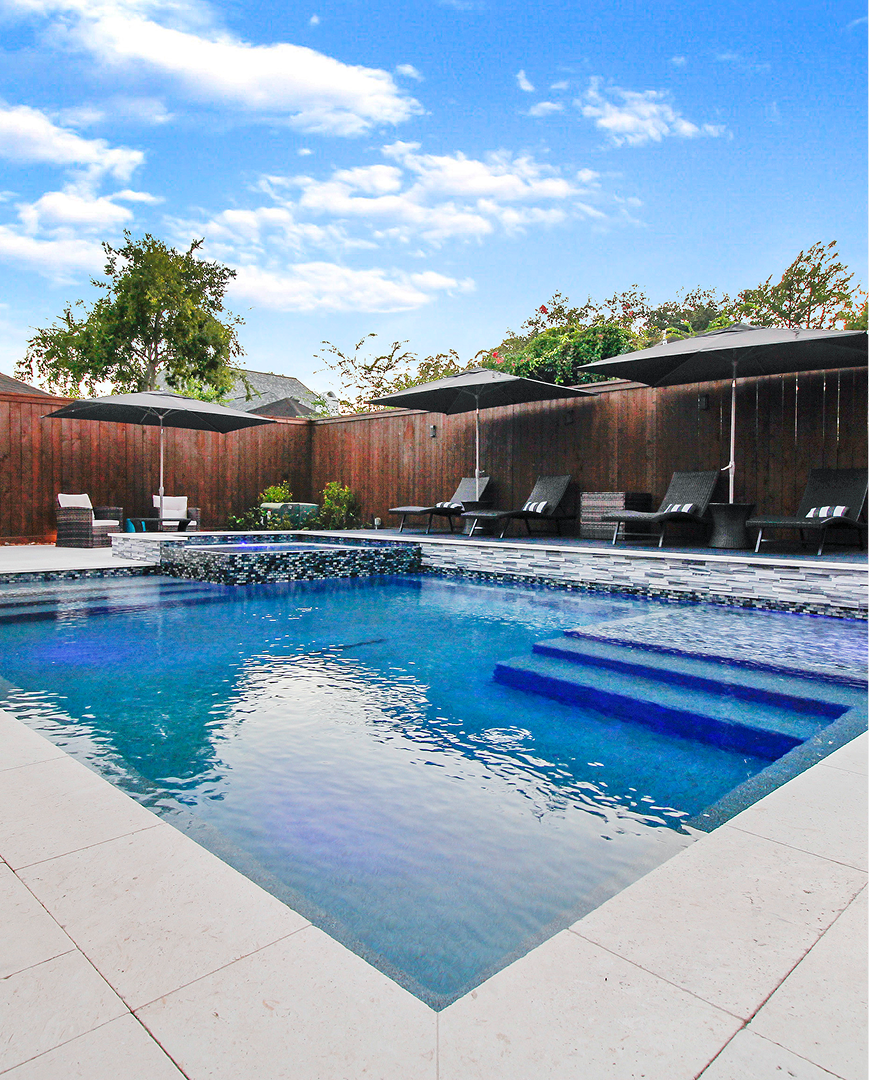Backyard pool with blue water, lounge chairs, wooden fence, and a sunny sky