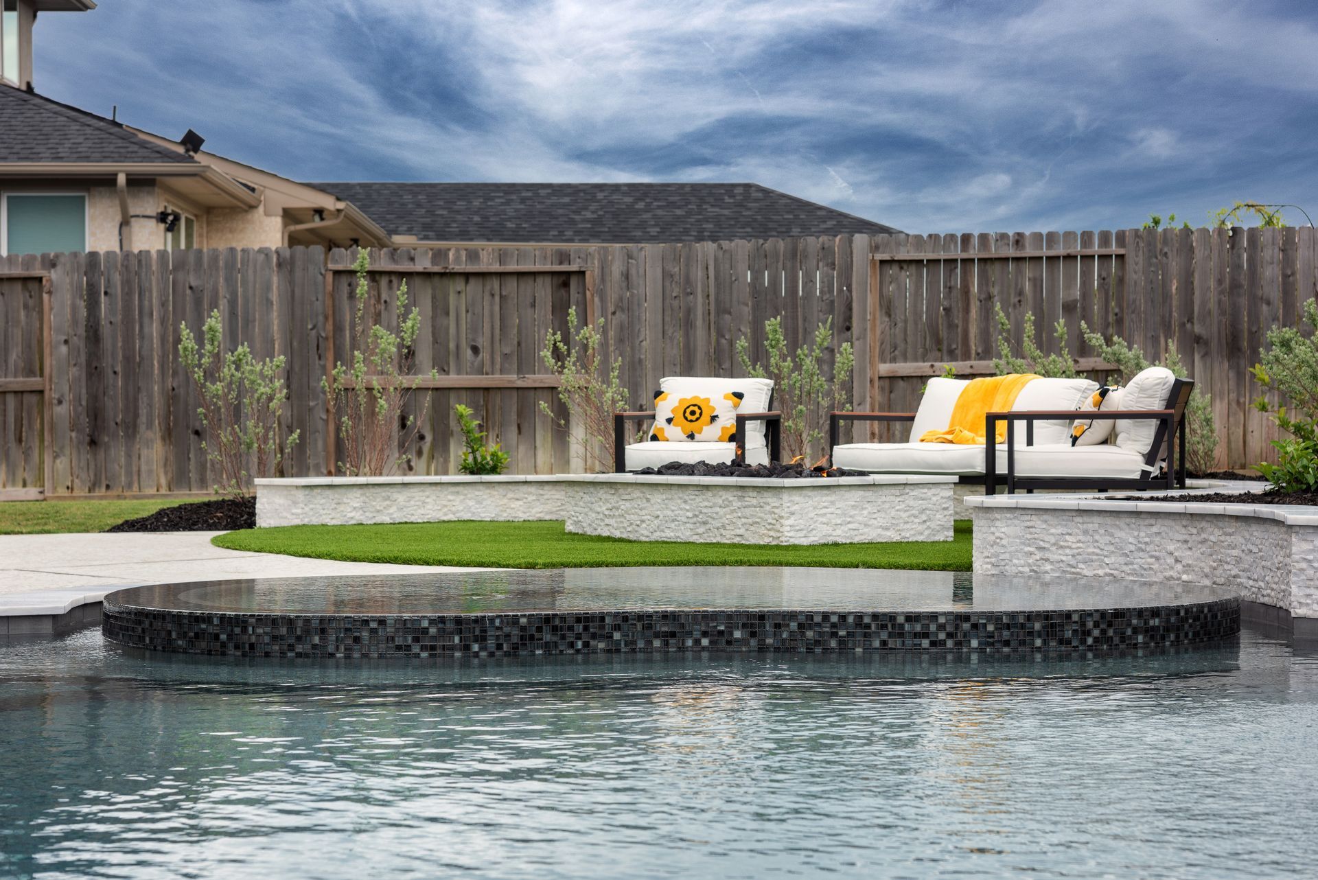 Outdoor resort pool with clear blue water, tiled steps, and lounge chairs under trees at sunset
