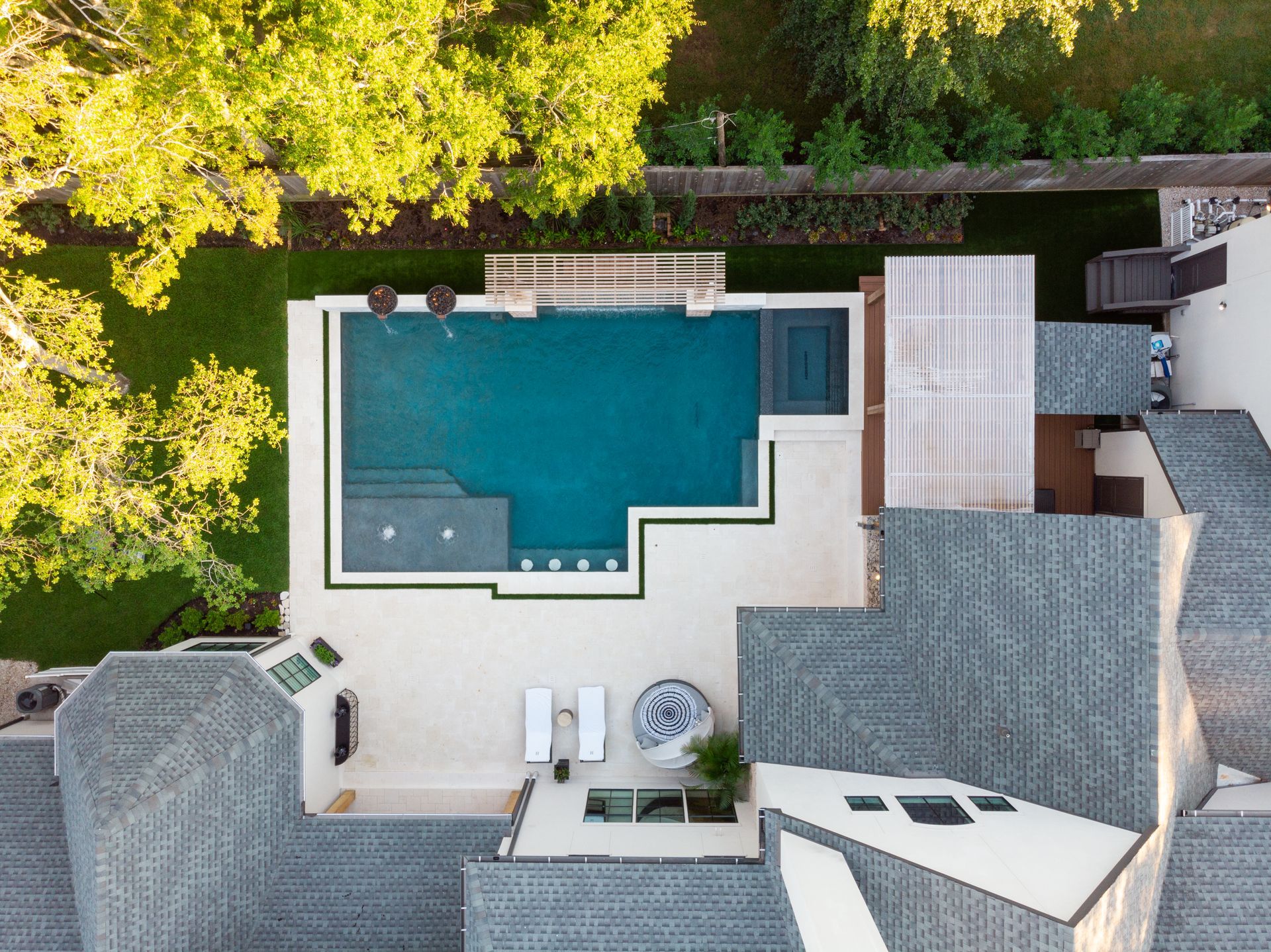 Modern outdoor pool with clear water, blue mosaic tiles, and lounge chairs beside trees under a blue sky