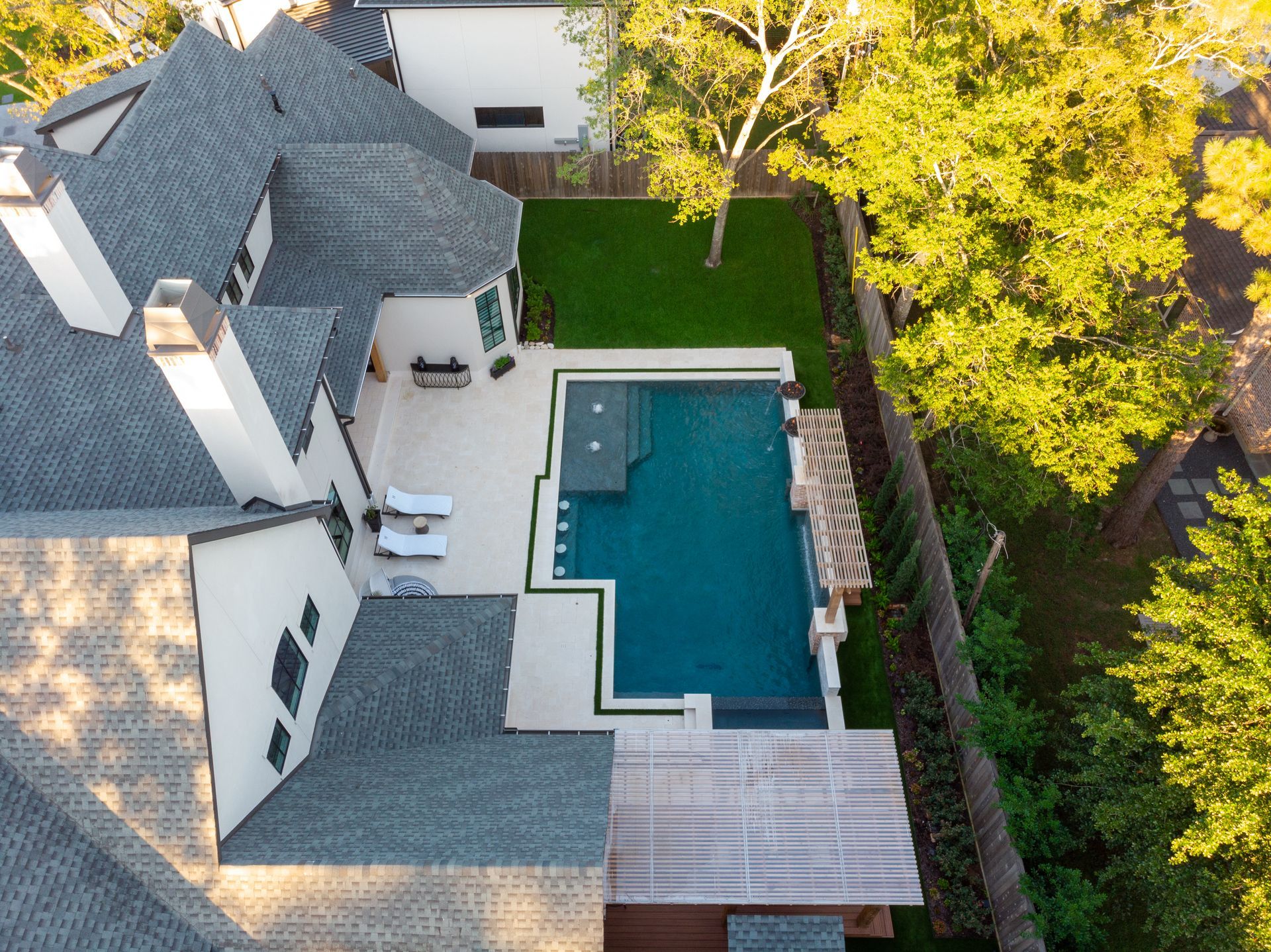 Backyard pool with a square hot tub, stone deck, and tall trees in the background.