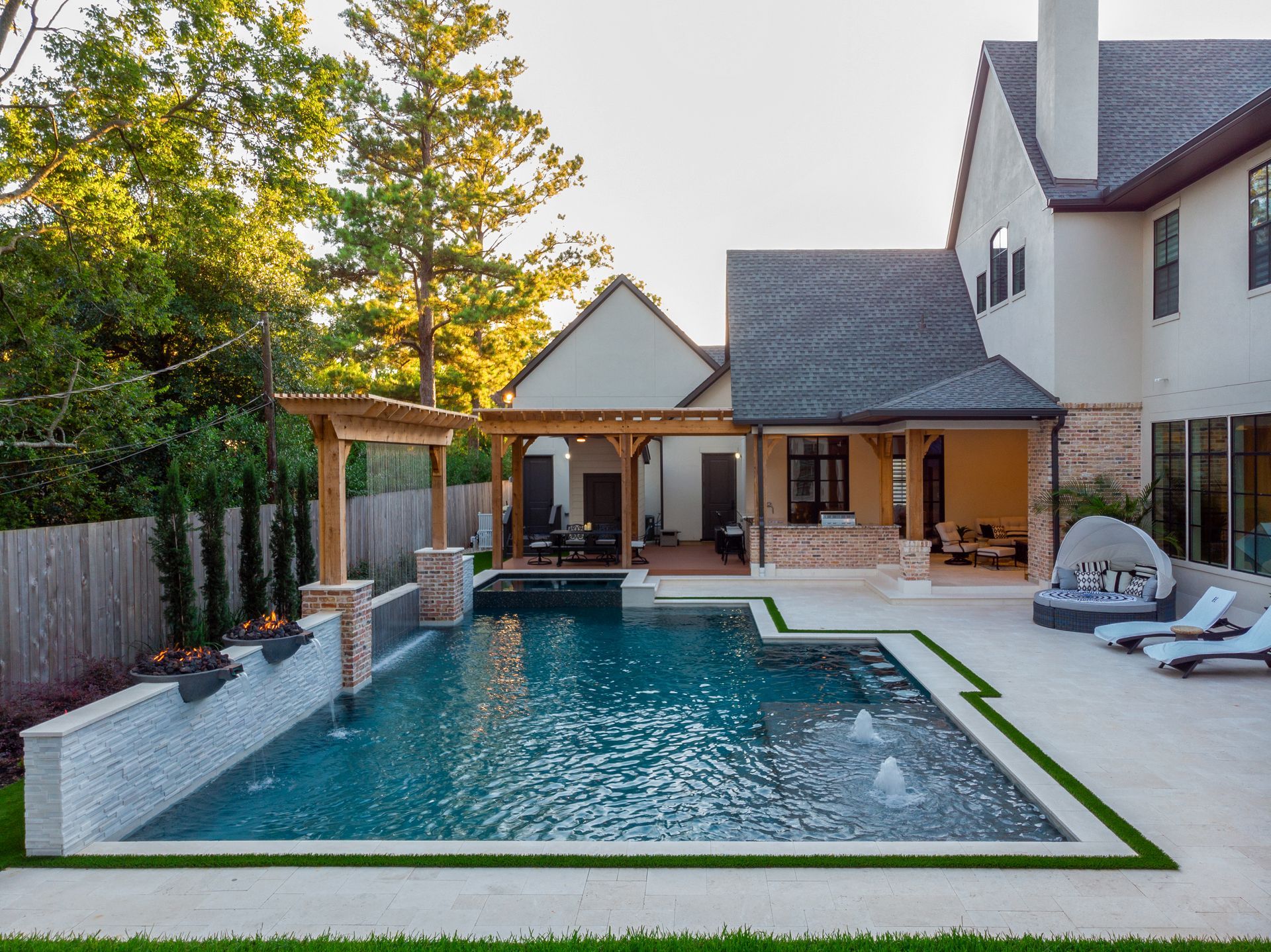 Modern outdoor pool with clear water, blue mosaic tiles, and lounge chairs under trees at sunset