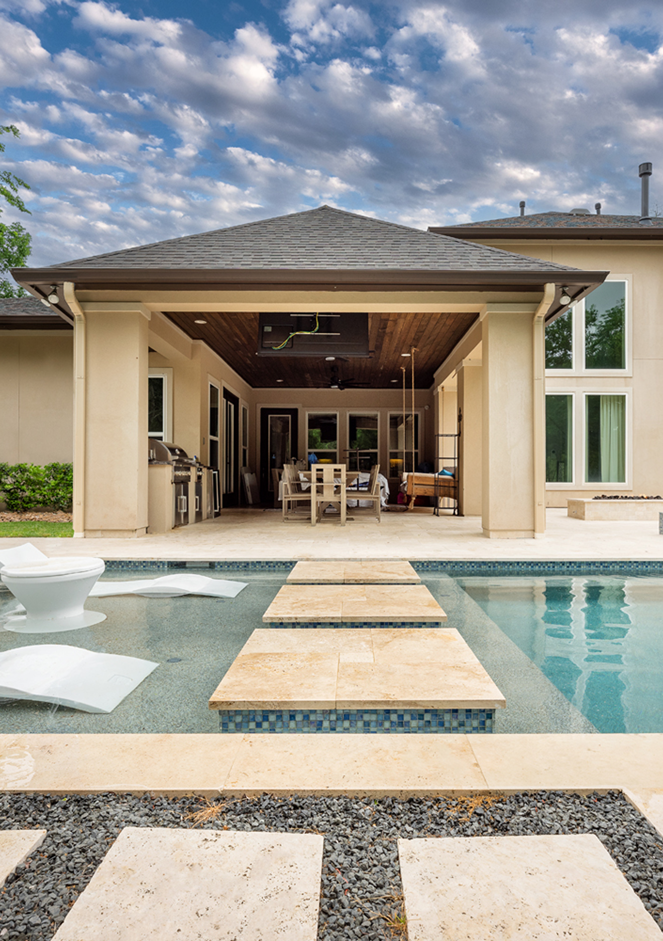 Backyard pool with stone stepping pads leading to a covered patio and outdoor seating area