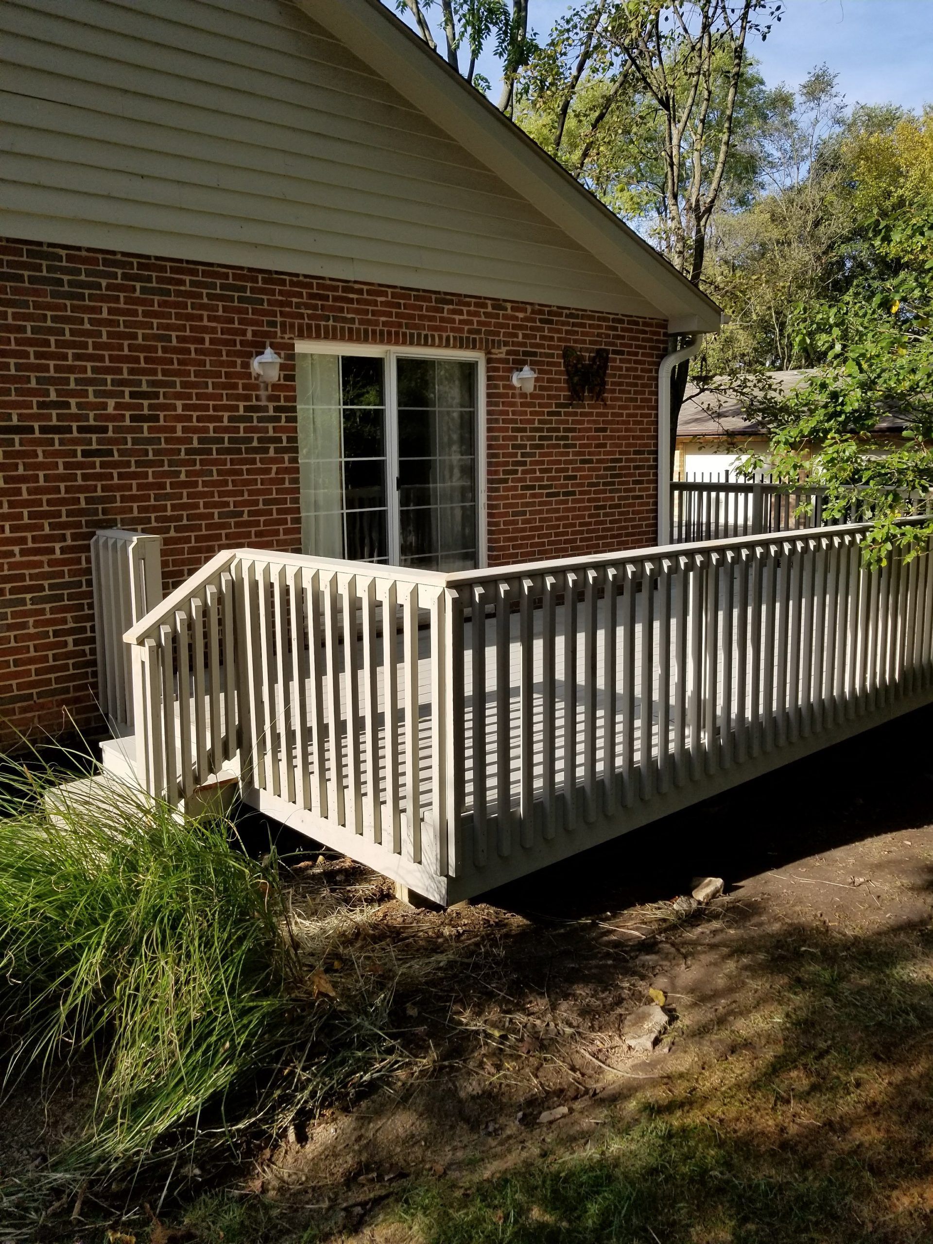 Wooden deck attached to a brick building, surrounded by green foliage.