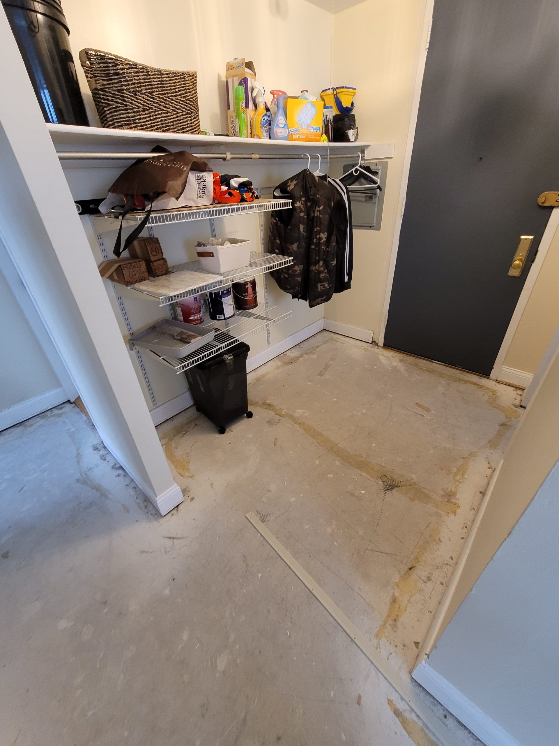 Laundry room with shelving, clothes rack, and gray door. Concrete floor.