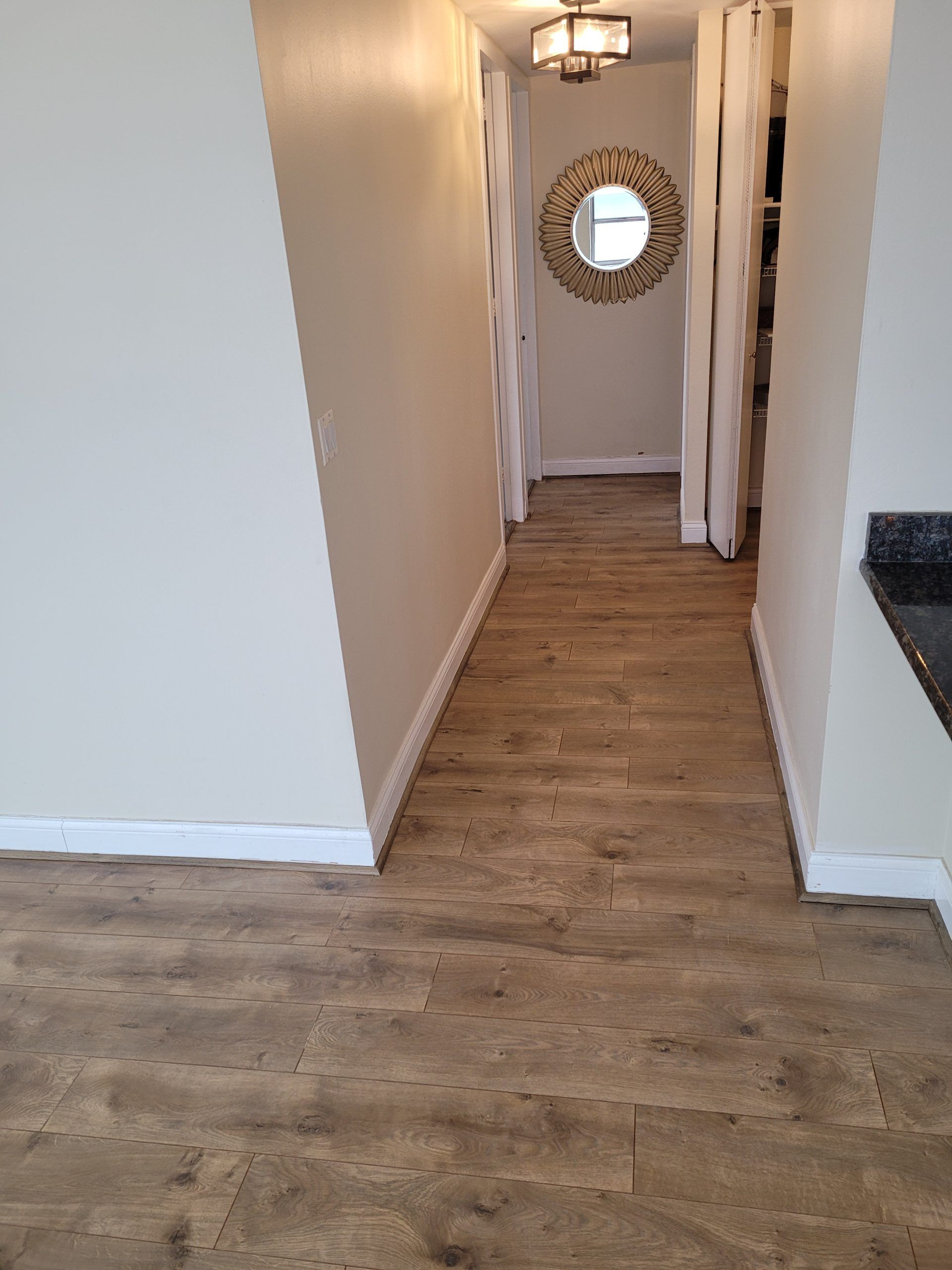 Hallway with wood-look flooring, light-colored walls, and a decorative mirror at the end.