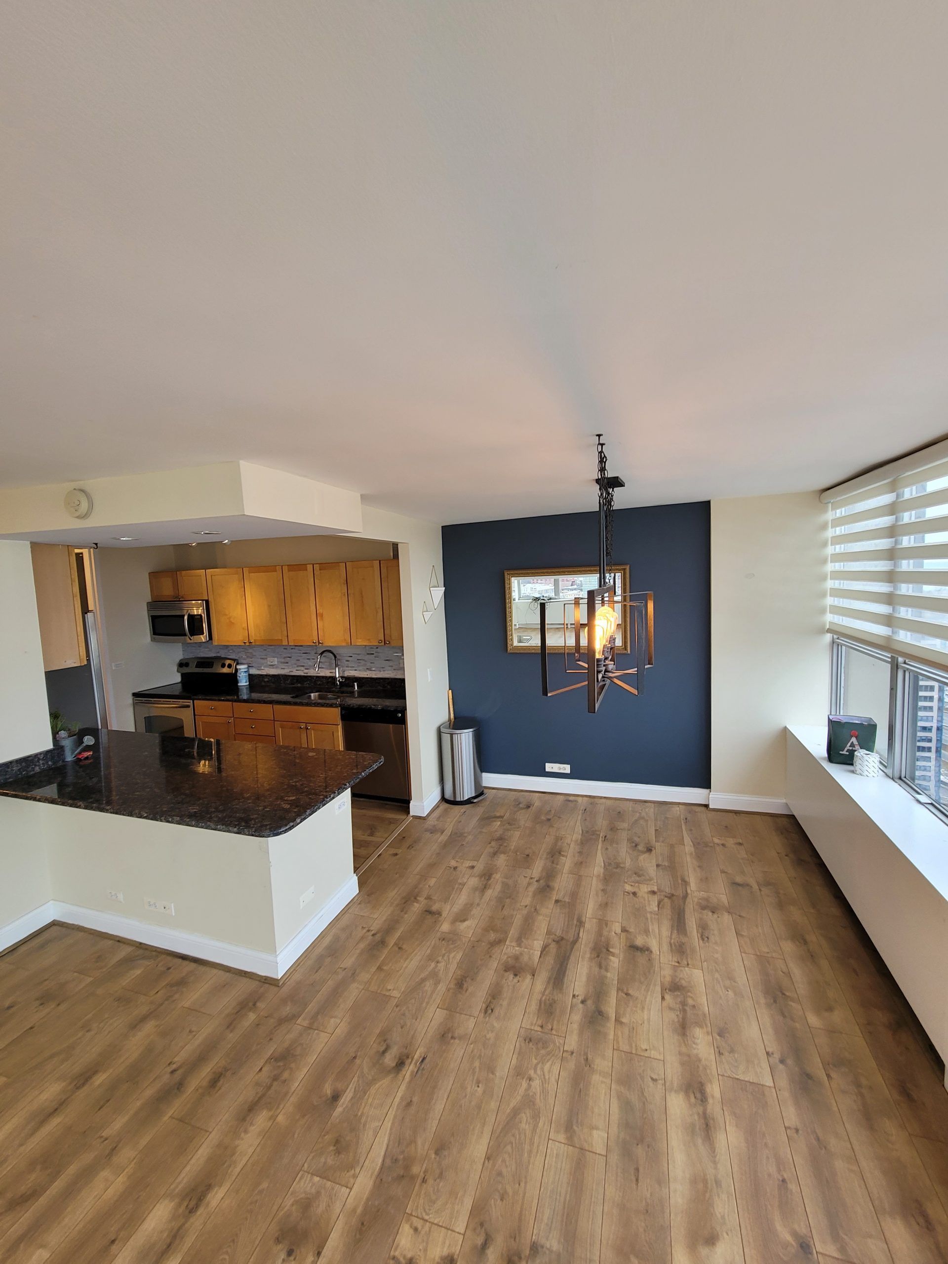 Open-concept living space with a kitchen, dark accent wall, wooden floors, and a pendant light fixture.