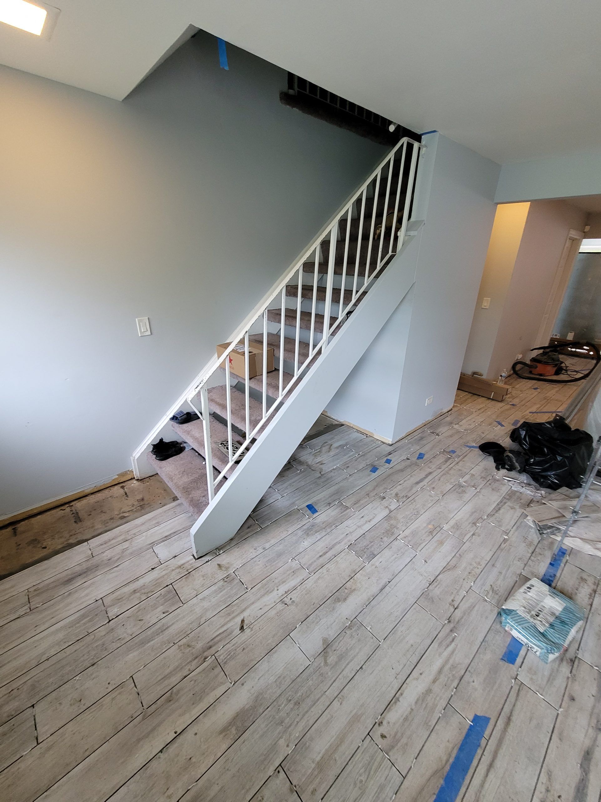 Staircase with white railing and light wood-look flooring. Light blue walls, construction materials on the floor.