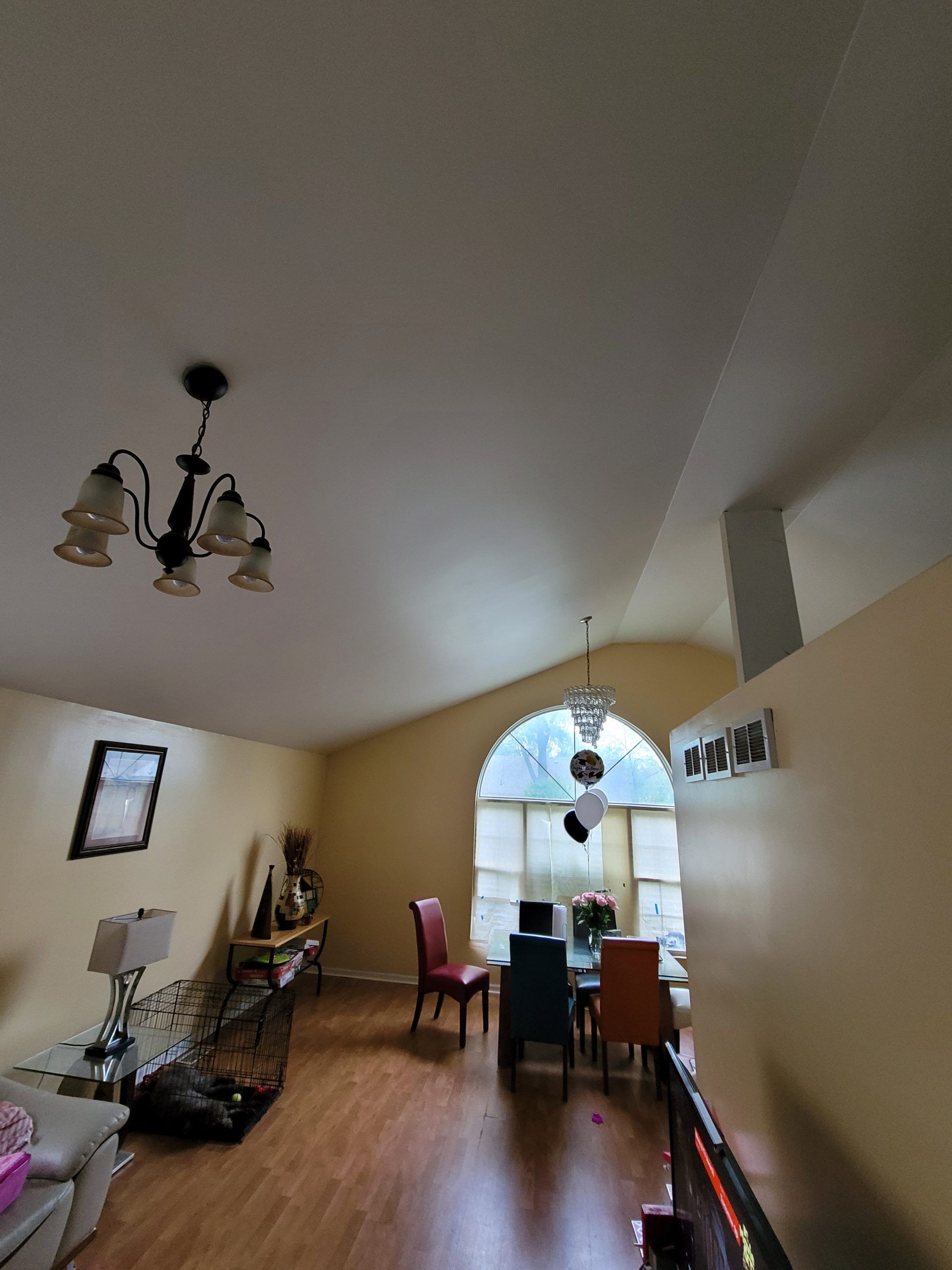 Dining room with chandelier, arched window, and table with chairs; wooden floor.