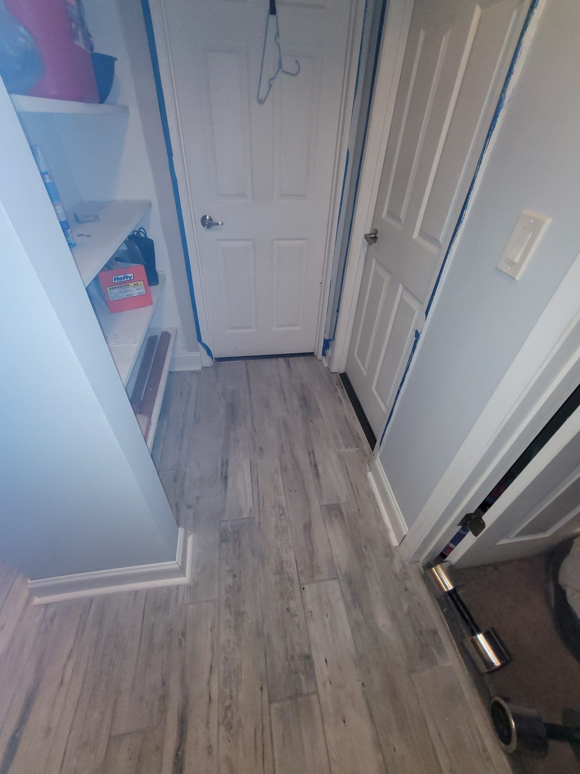 Narrow hallway with gray wood-look flooring, white doors, and a closet with shelves on the left.