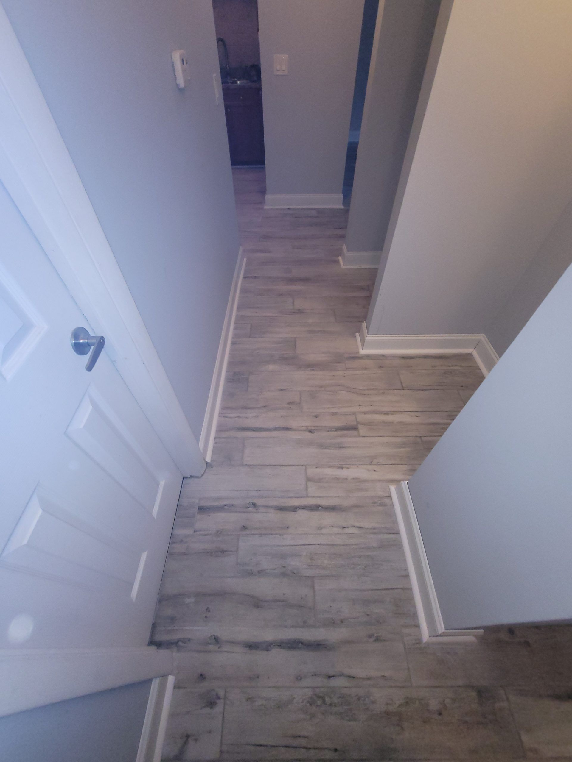 Hallway with light wood-look flooring, light gray walls, and white trim. Door on the left.