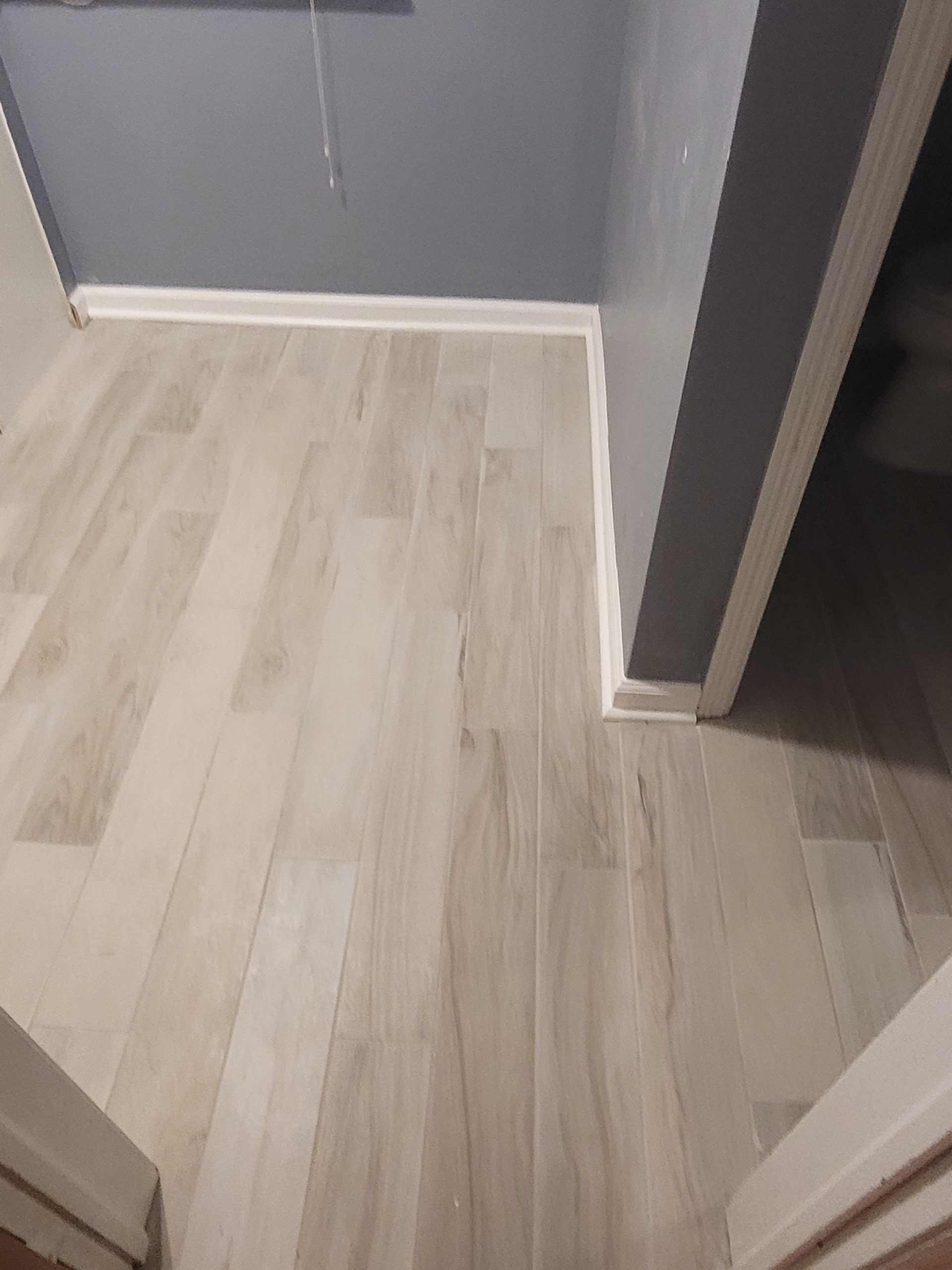 Light wood-look flooring in a bathroom. Gray wall above white baseboard. Door frames visible.
