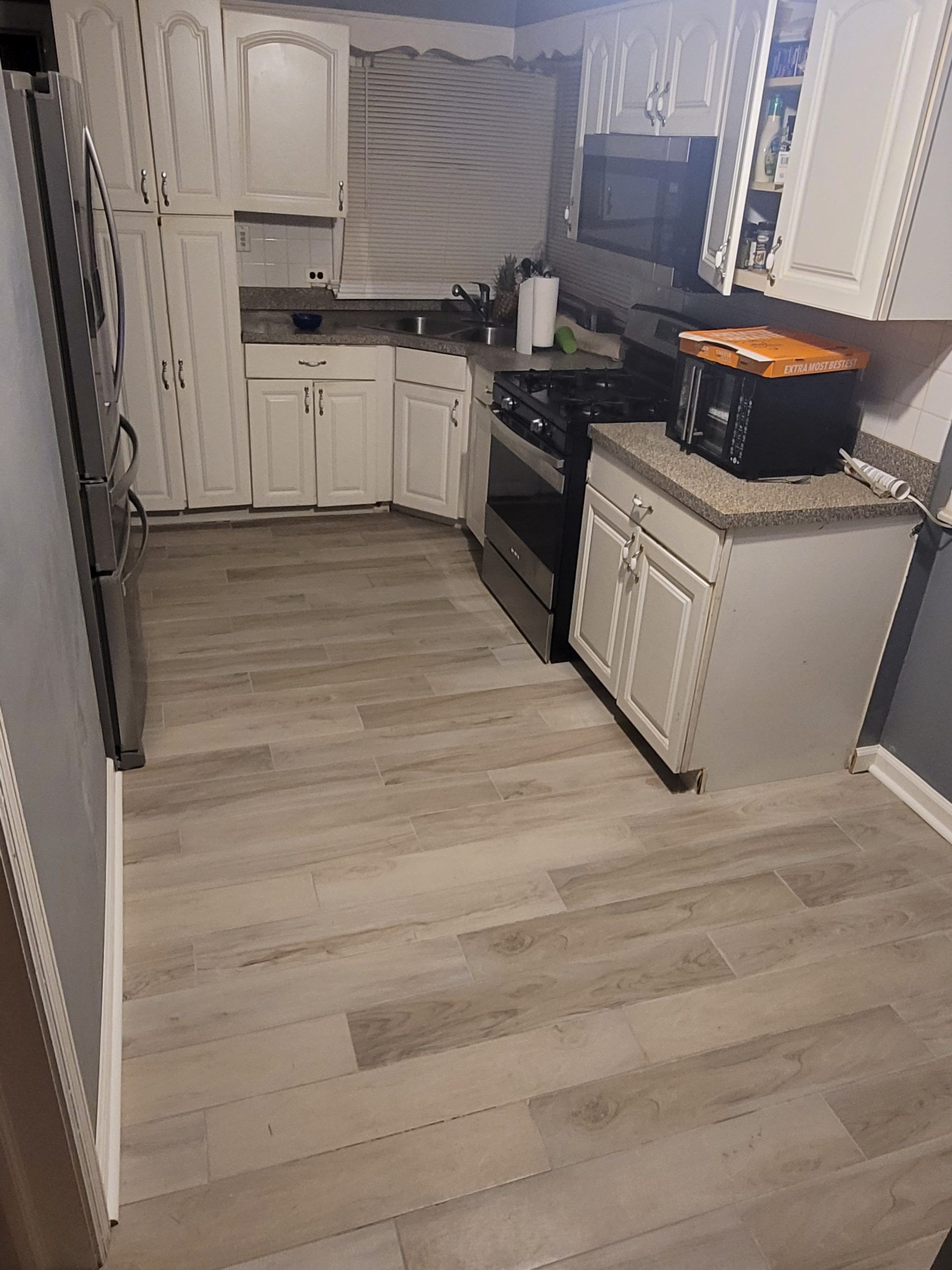 Kitchen with white cabinets, light wood-look flooring, stainless steel appliances, and a microwave on the countertop.