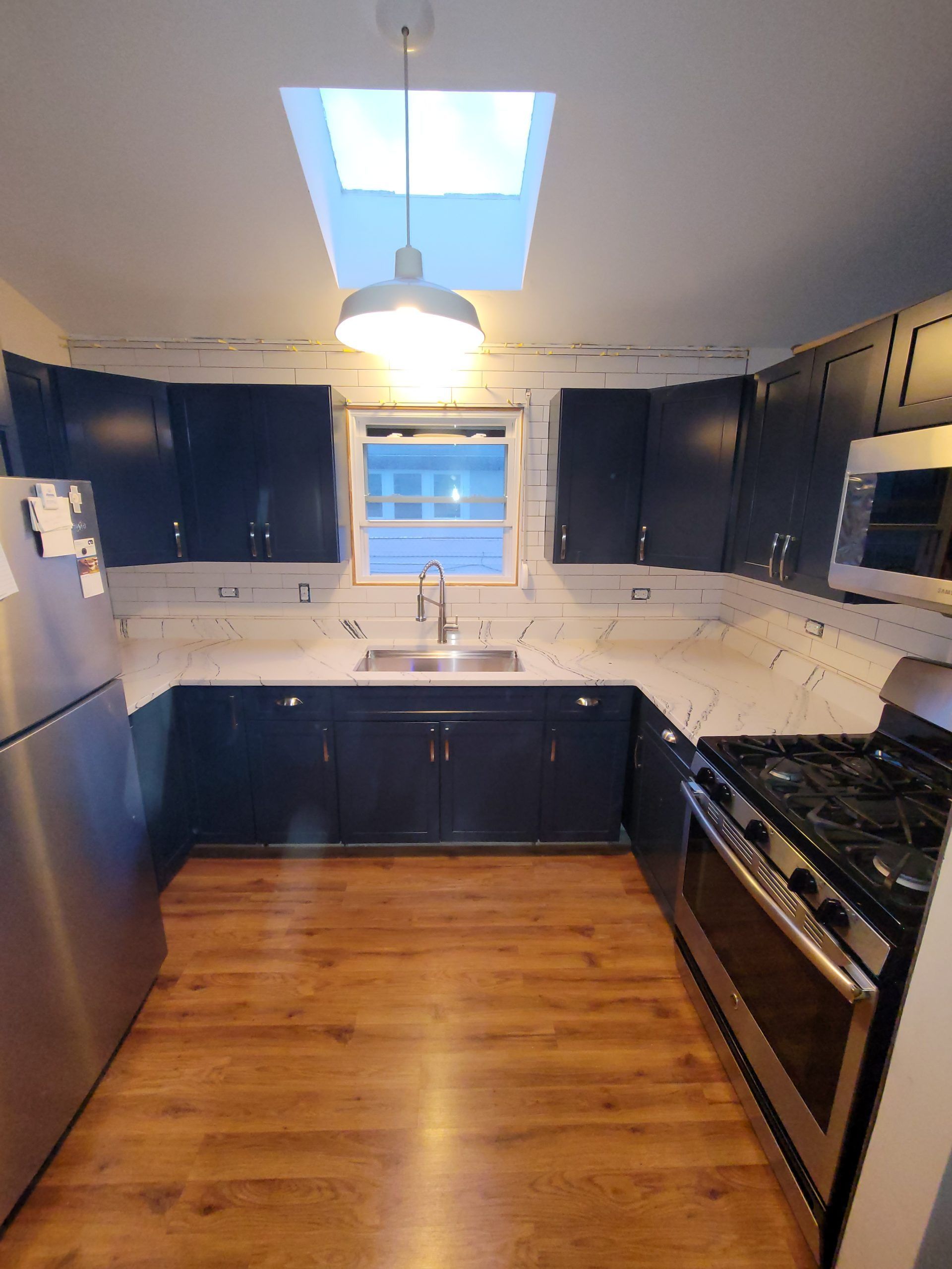 Dark blue kitchen cabinets, white countertops, stainless steel appliances, and wooden floors.