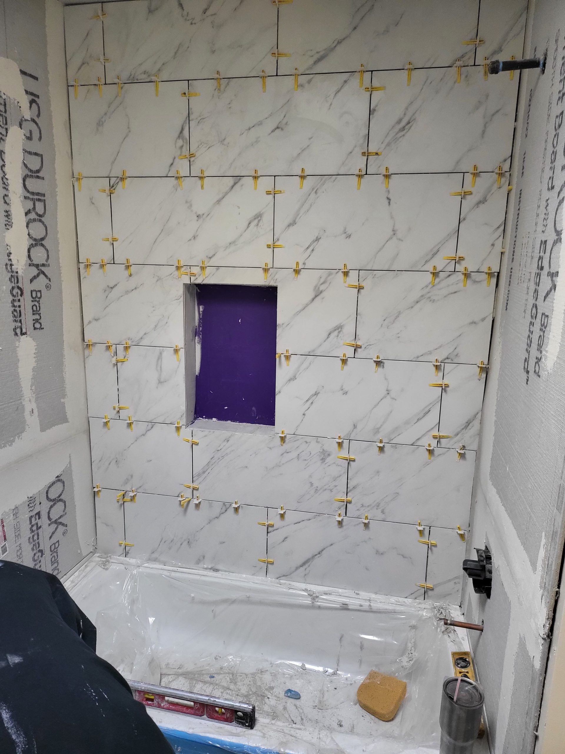 Bathroom with white marbled tiles, purple niche, and tile spacers.