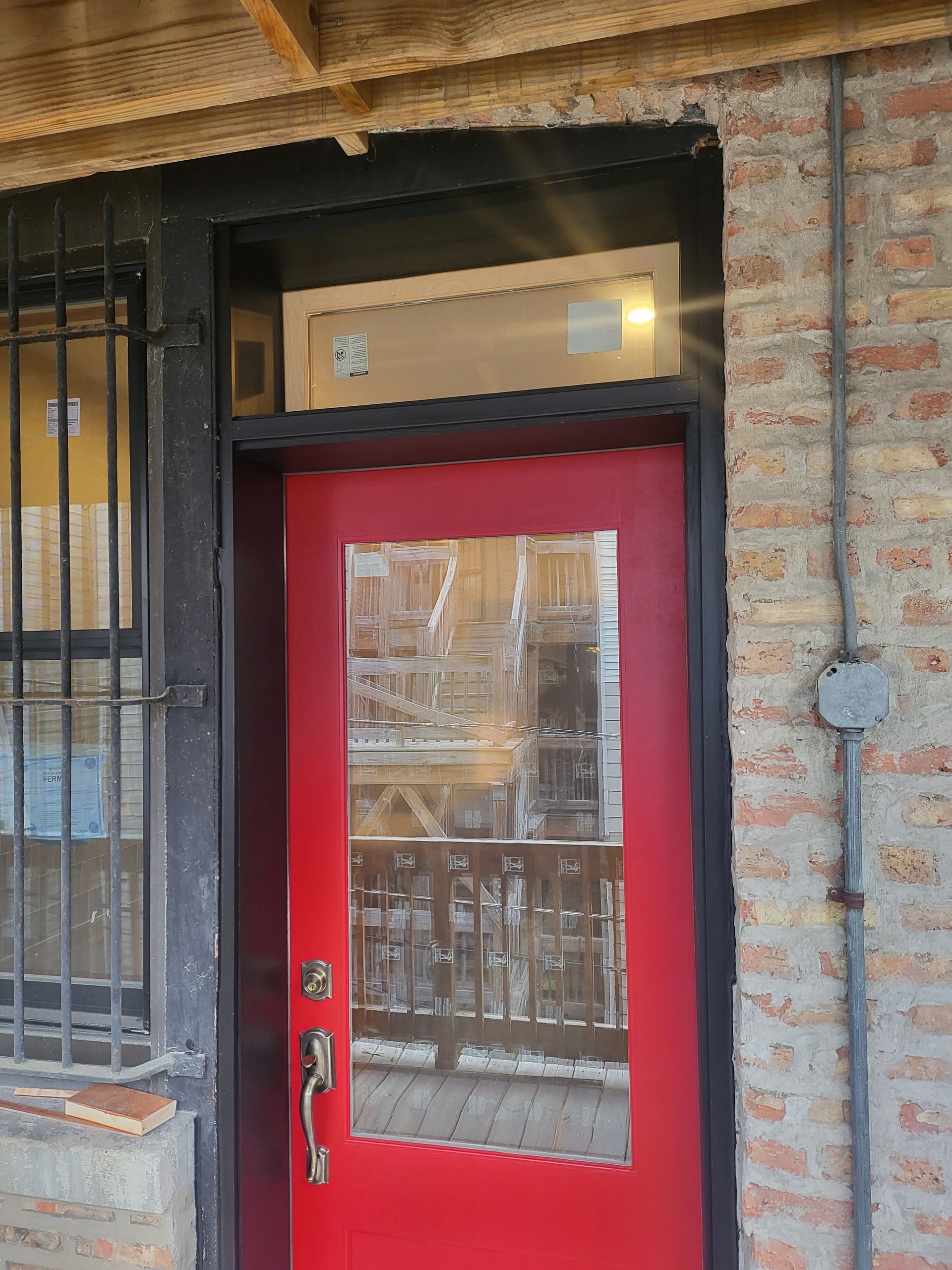 Red door with glass panel, black frame, brick wall, and window with security bars.