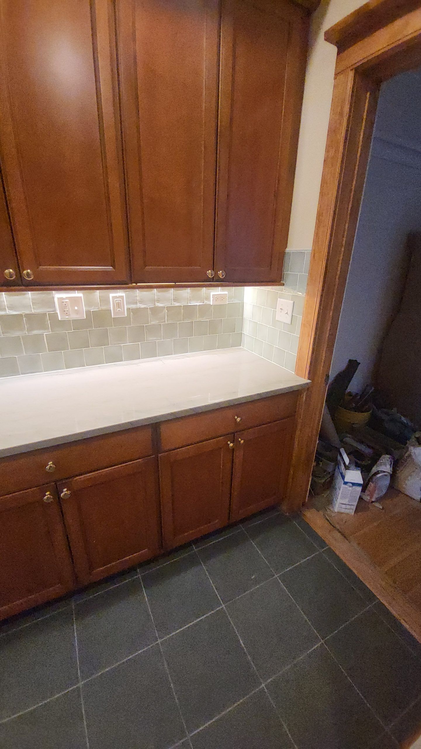 Kitchen cabinets with a light countertop and backsplash, dark floor, and an open doorway.
