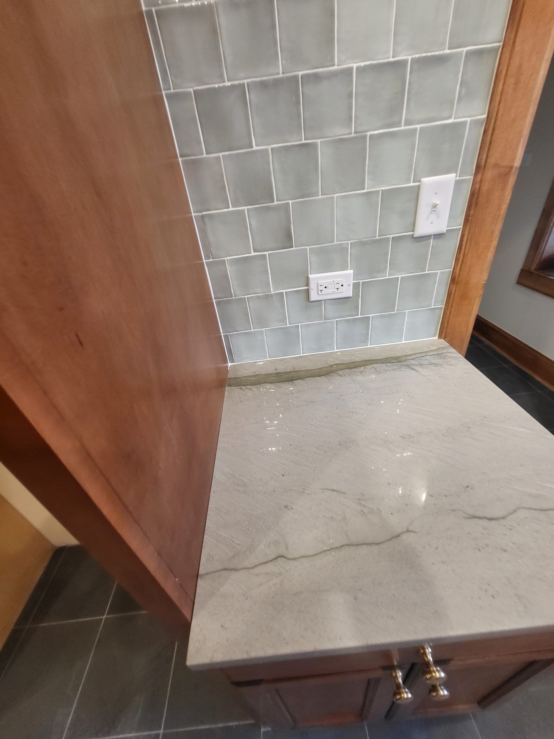 Kitchen counter with gray quartz surface, tile backsplash, and wooden cabinetry.