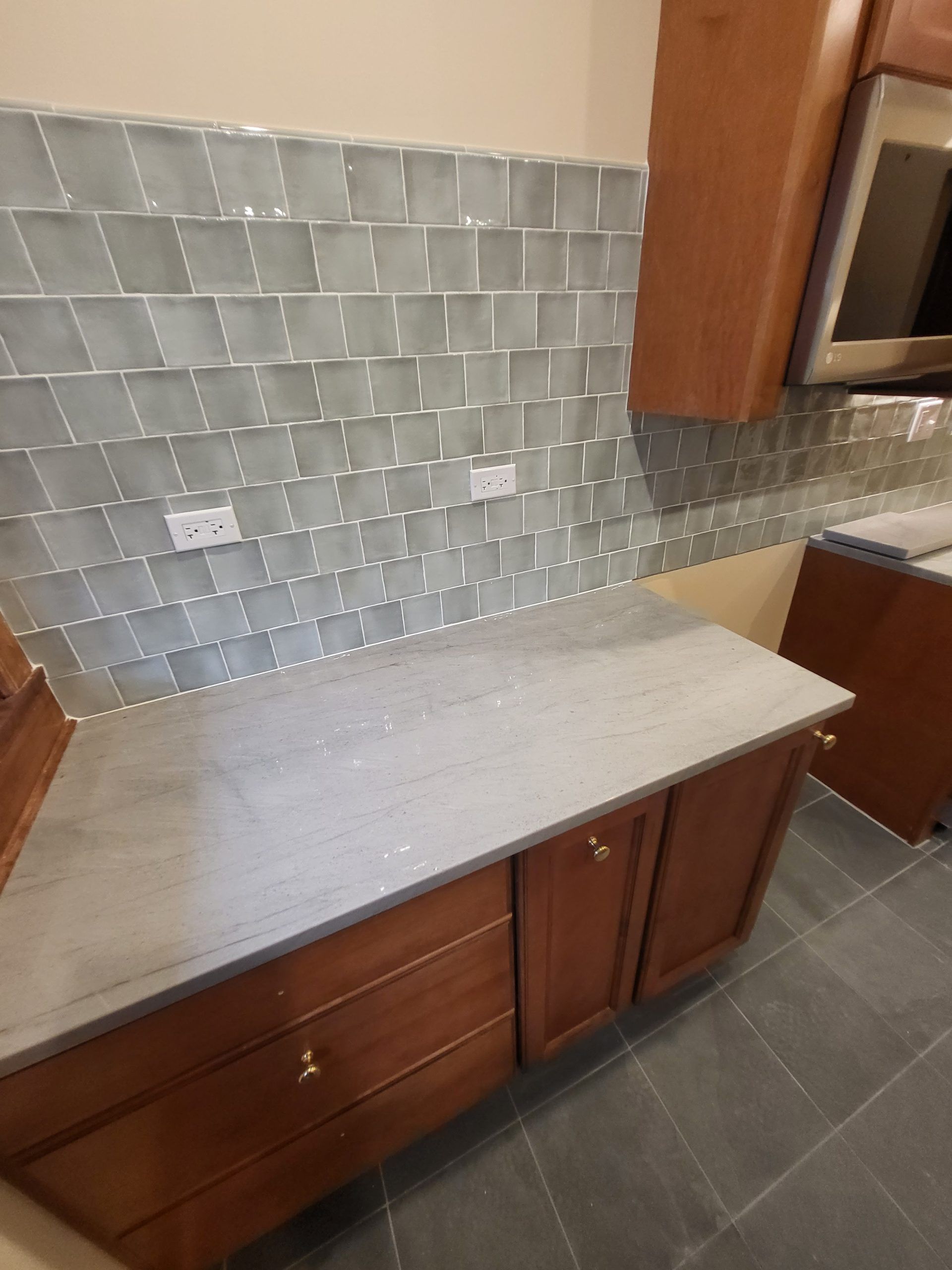 Kitchen with gray countertop, wooden cabinets, and glass tile backsplash.