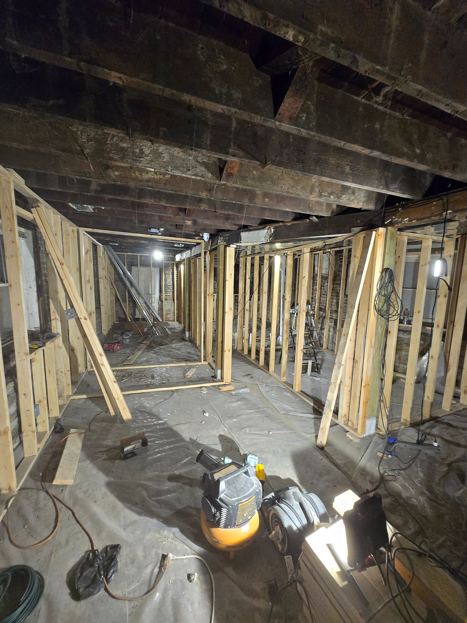 Renovated home interior: demolished flooring debris, staircase, open door, worker in the background.