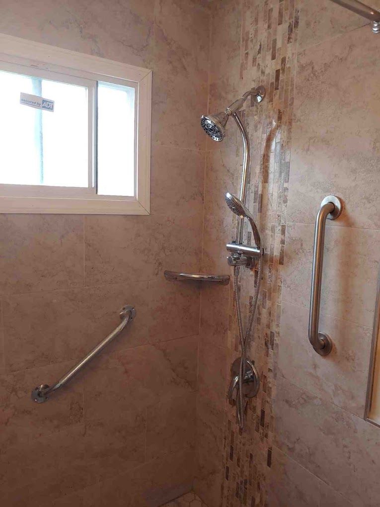 Shower with grab bars, showerhead, and window. Beige tile walls with decorative strip.