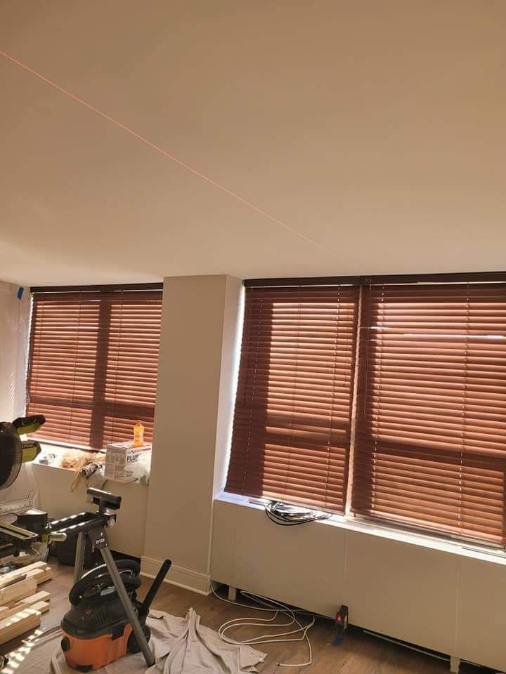 Room with three windows, brown blinds, and a white pillar. A red laser line is visible on the ceiling.
