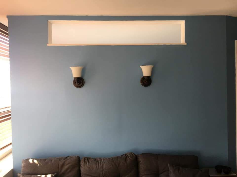 Blue wall with a recessed white shelf, two sconces, and a gray couch.
