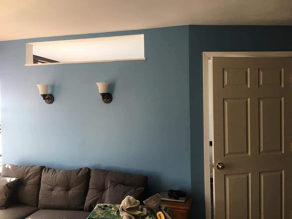 Blue-painted wall with a recessed shelf, two sconces, and a closed door. A couch is in the foreground.