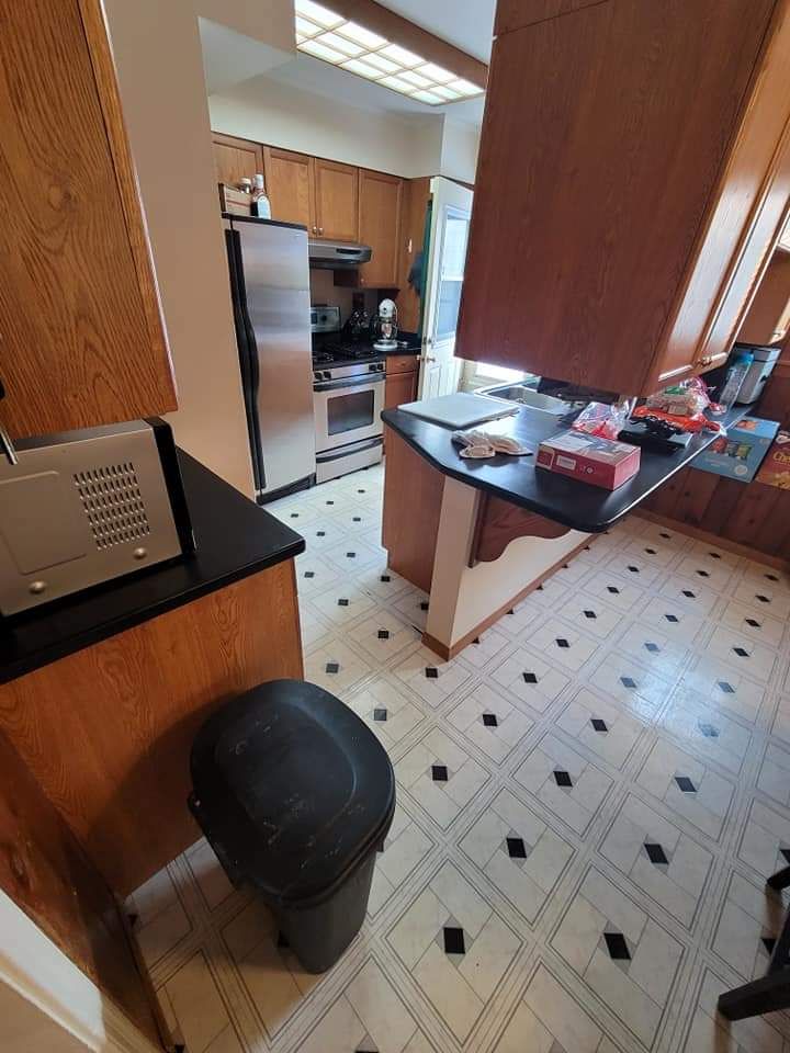 Kitchen with wooden cabinets, black countertops, stainless steel appliances, and black and white tile flooring.
