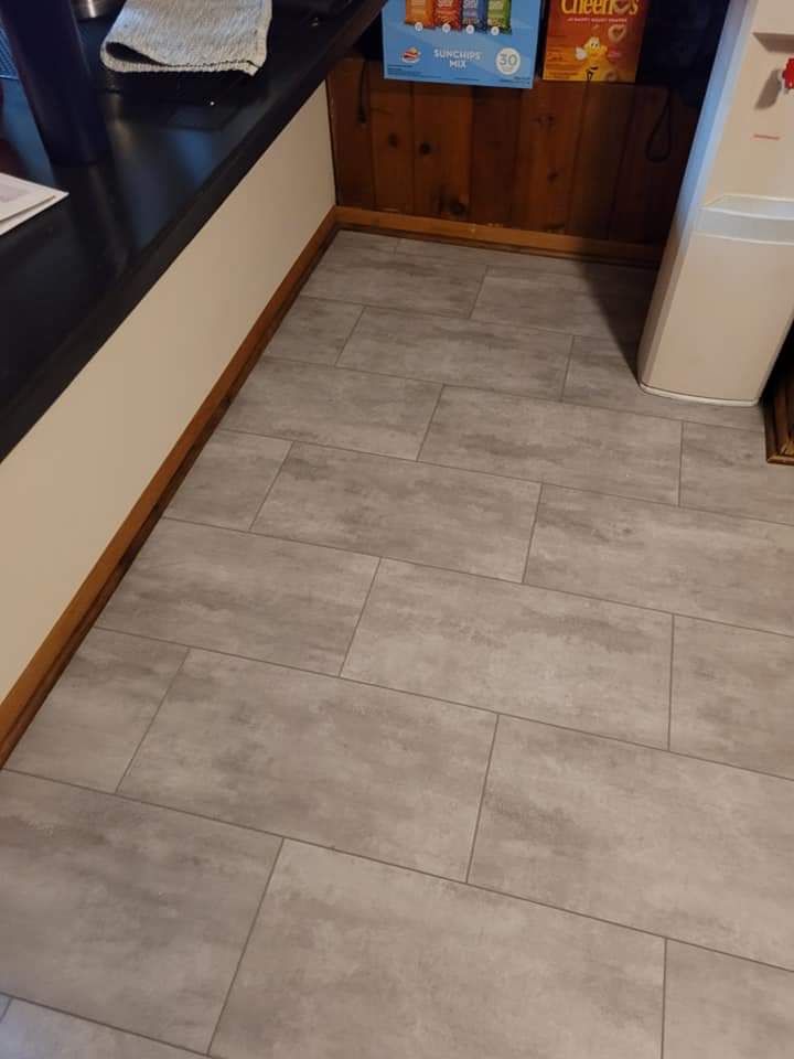 Gray tile flooring in a room with a black counter, wood paneling, and a white appliance.