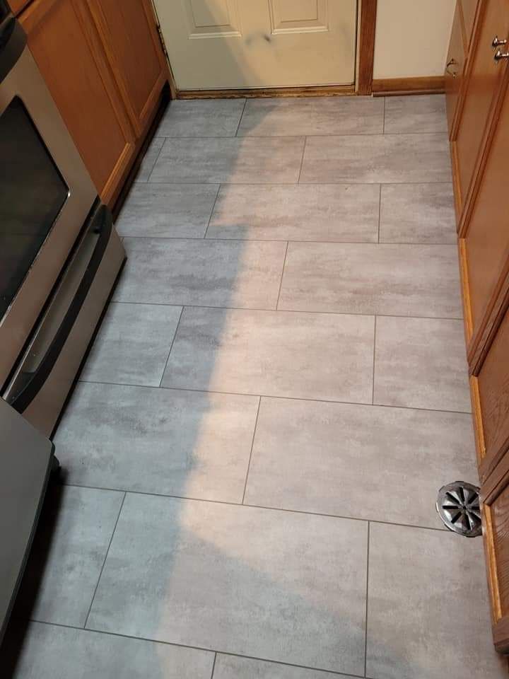 Kitchen floor with gray rectangular tiles, between cabinets and a stove.