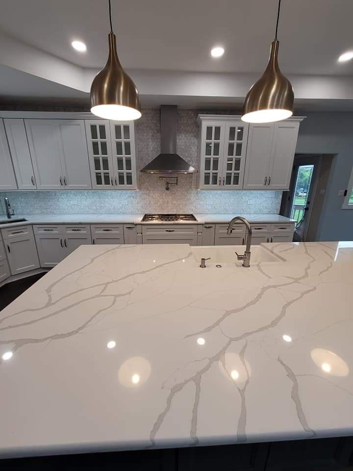 Modern kitchen with white cabinets, marble countertop island, and brass pendant lights.