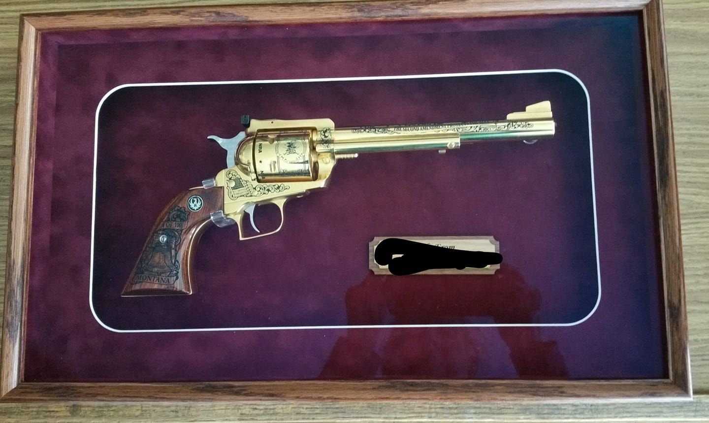 A picture of a gold revolver in a wooden frame