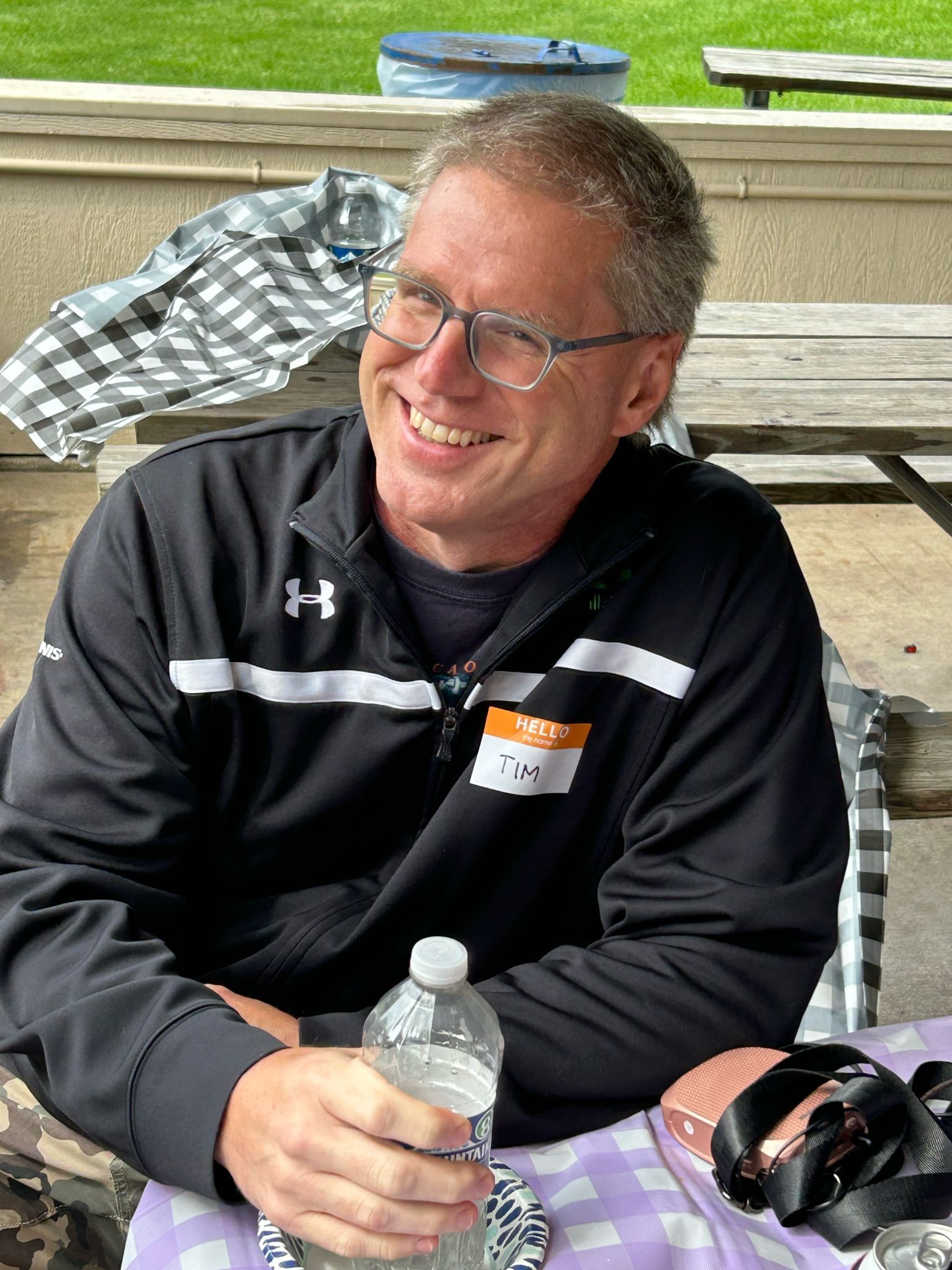 A man wearing glasses is sitting at a table holding a bottle of water.