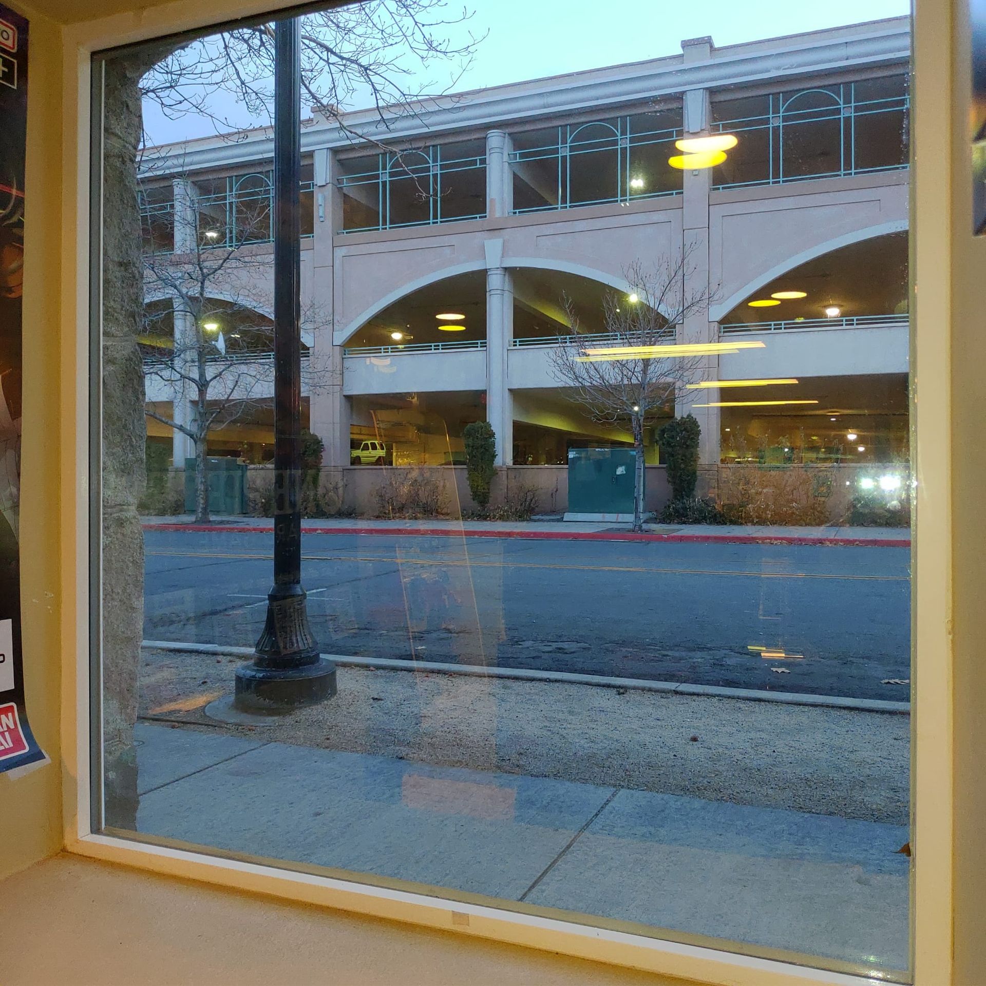 A view through a window looking out at a multi-level parking garage across a street with a lamp post in the foreground.