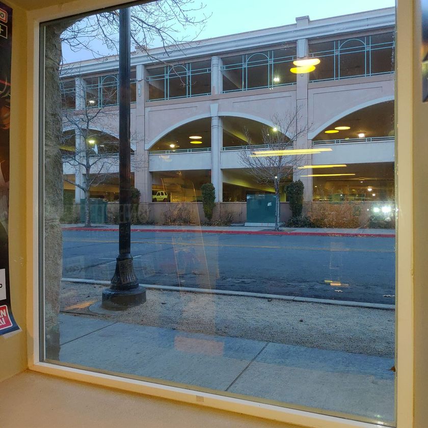 A view through a window showing a light-colored multi-level parking garage across a street with a lamp post.