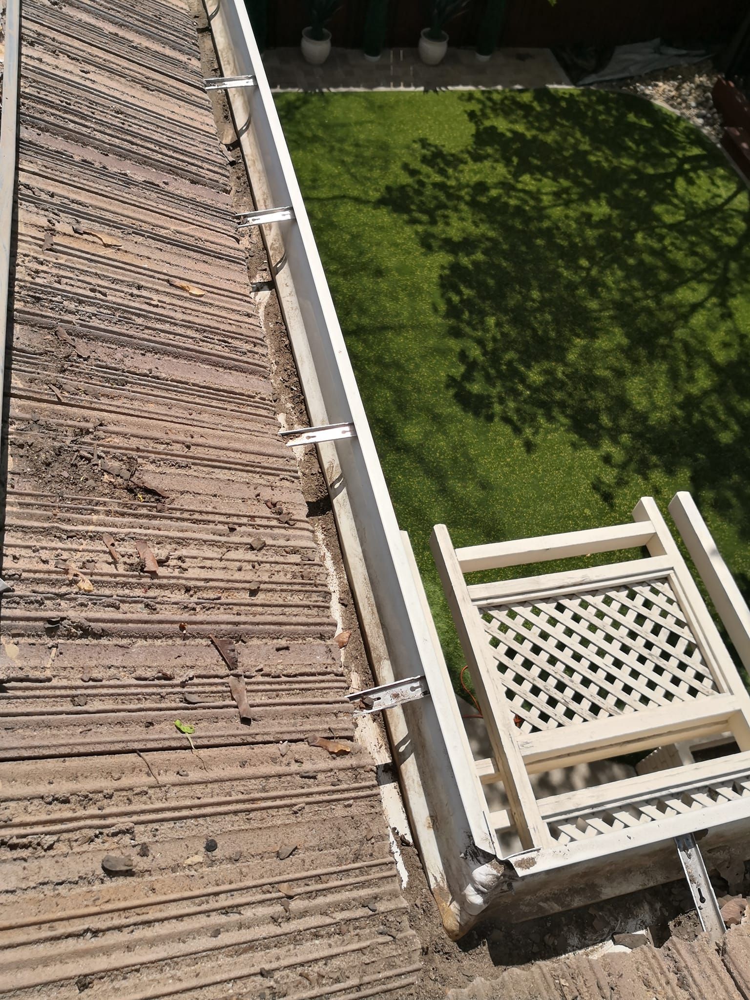 An elevated view of a corrugated brown roof with metal mounting brackets attached, overlooking a green backyard garden.