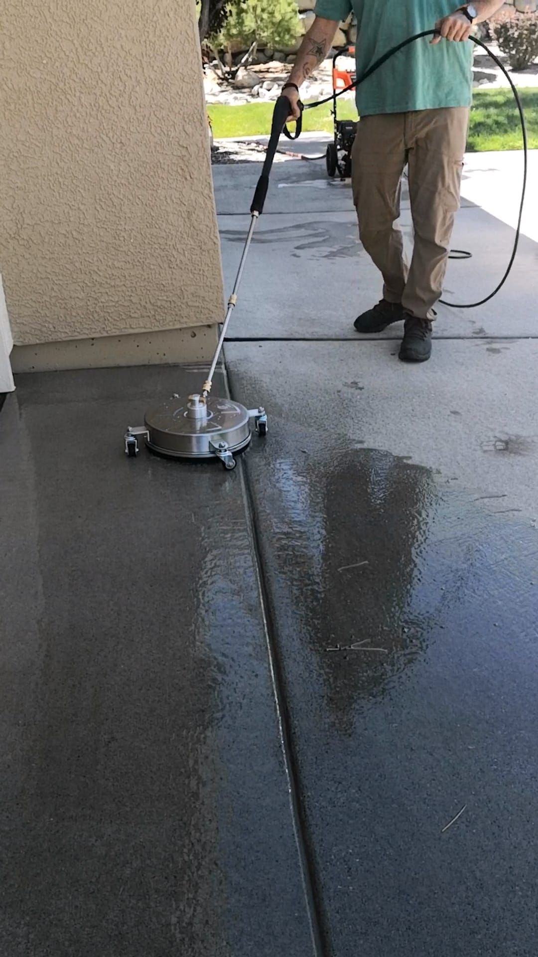 A person using a circular pressure washer surface cleaner on a concrete patio.