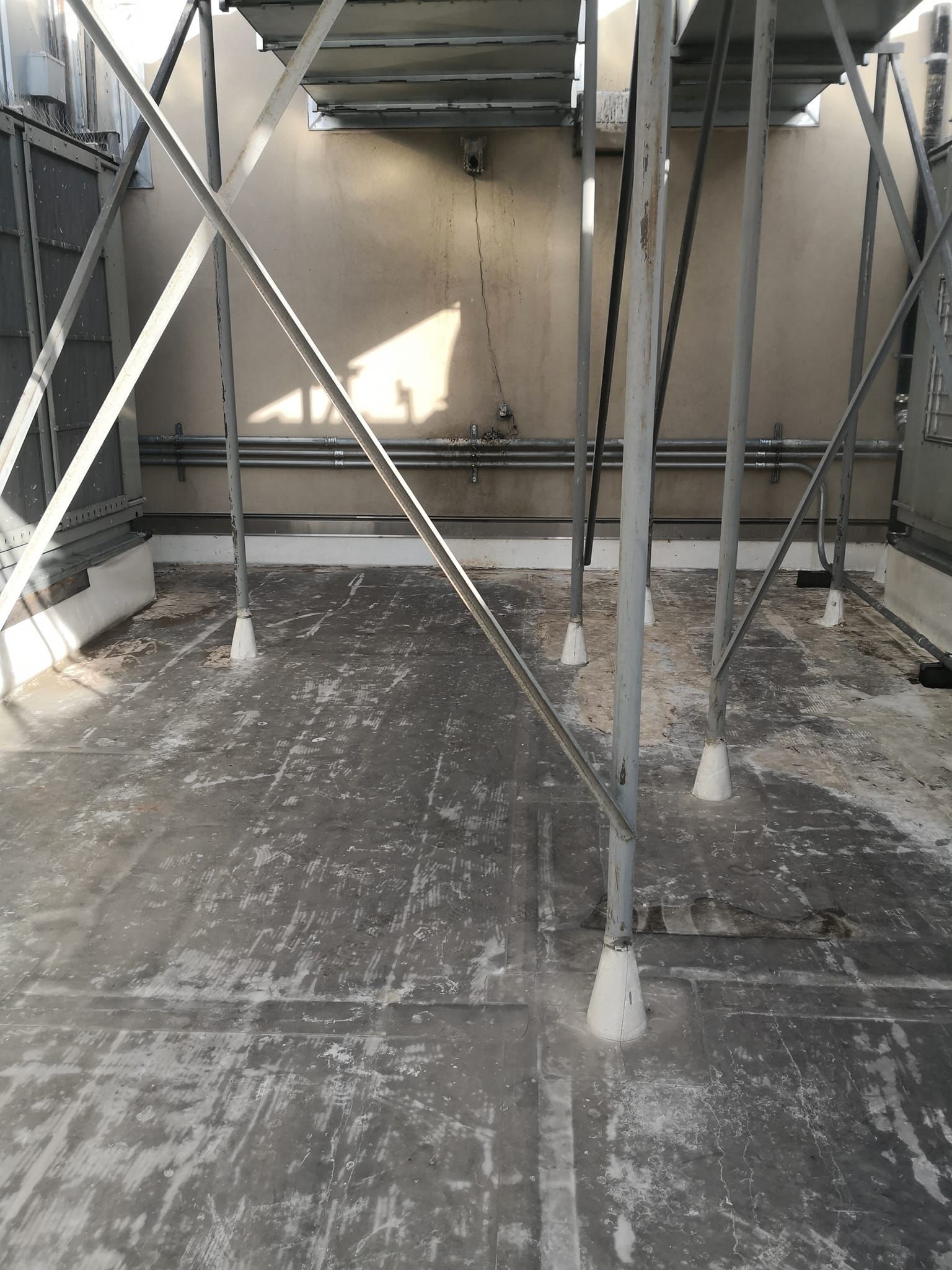 An outdoor rooftop area with several metal support posts, cross-braced poles, and a gray, weathered-looking floor.