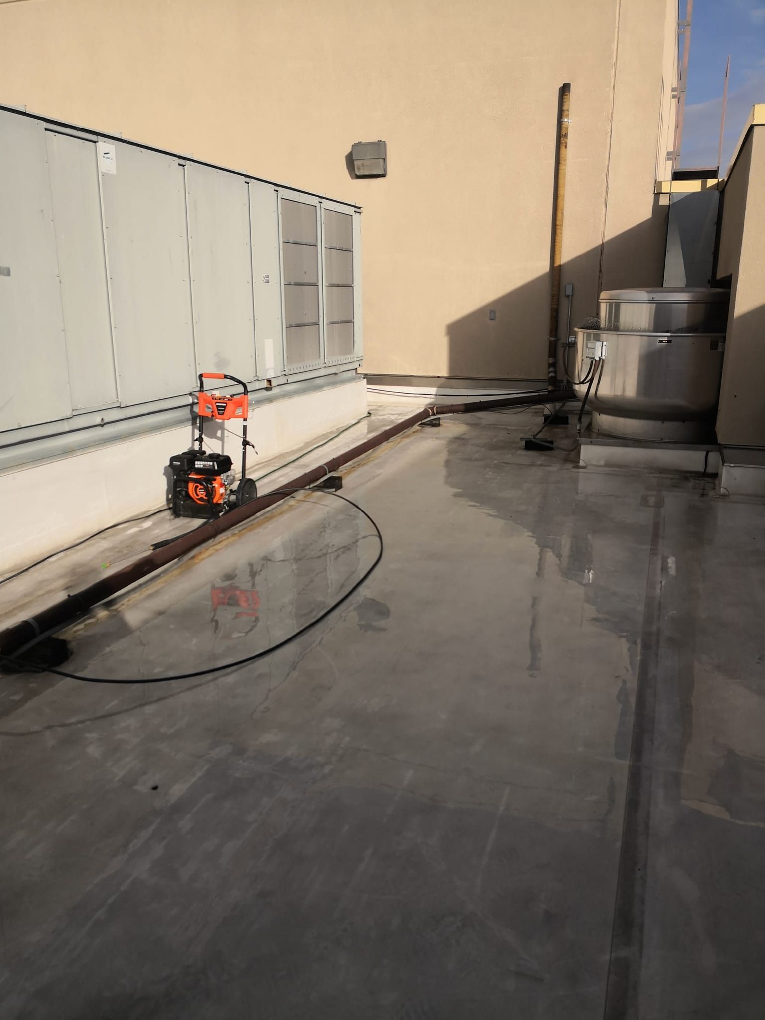 An orange portable power station sits on a flat roof next to a large HVAC unit and a metal exhaust fan.