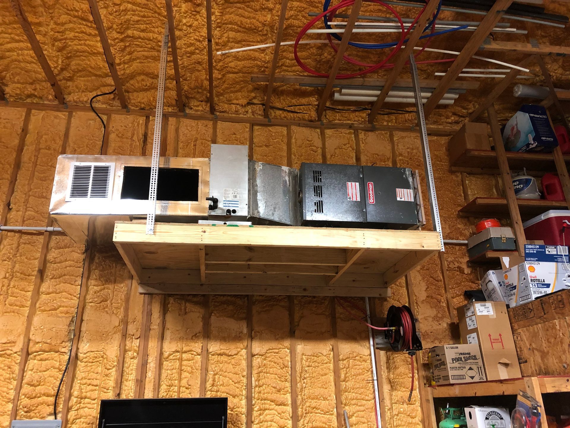 Garage attic with exposed rafters, a shelf of boxes, and a white appliance on a wooden platform