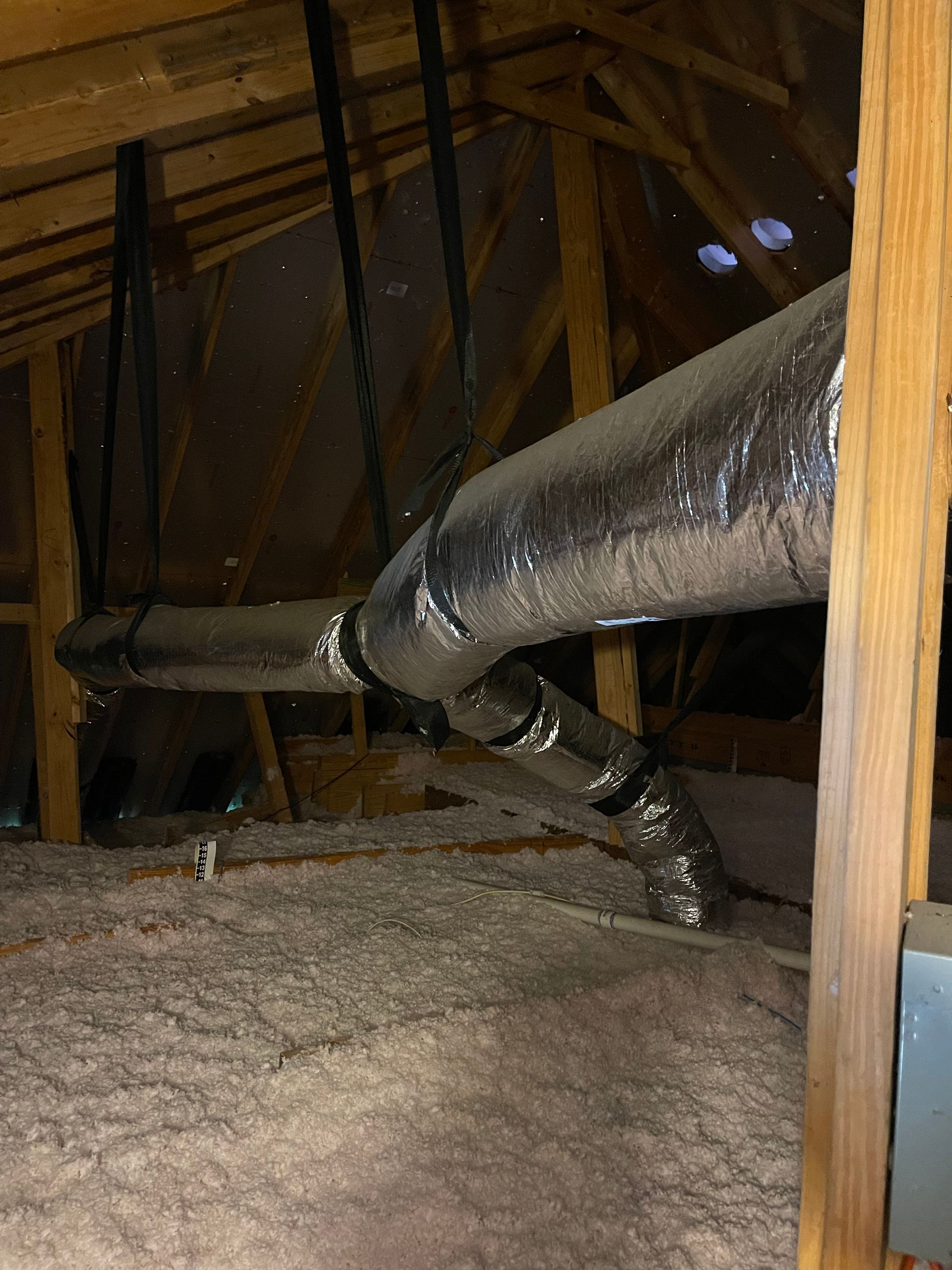Attic with exposed beams and insulated ductwork running across the ceiling.